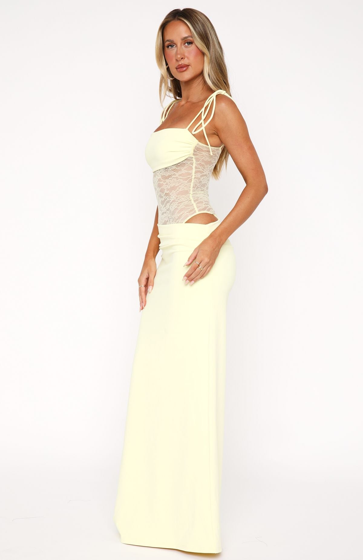 Side profile of the pale yellow Abigail lace maxi dress, highlighting the cut-out detail at the waist and flowing skirt.