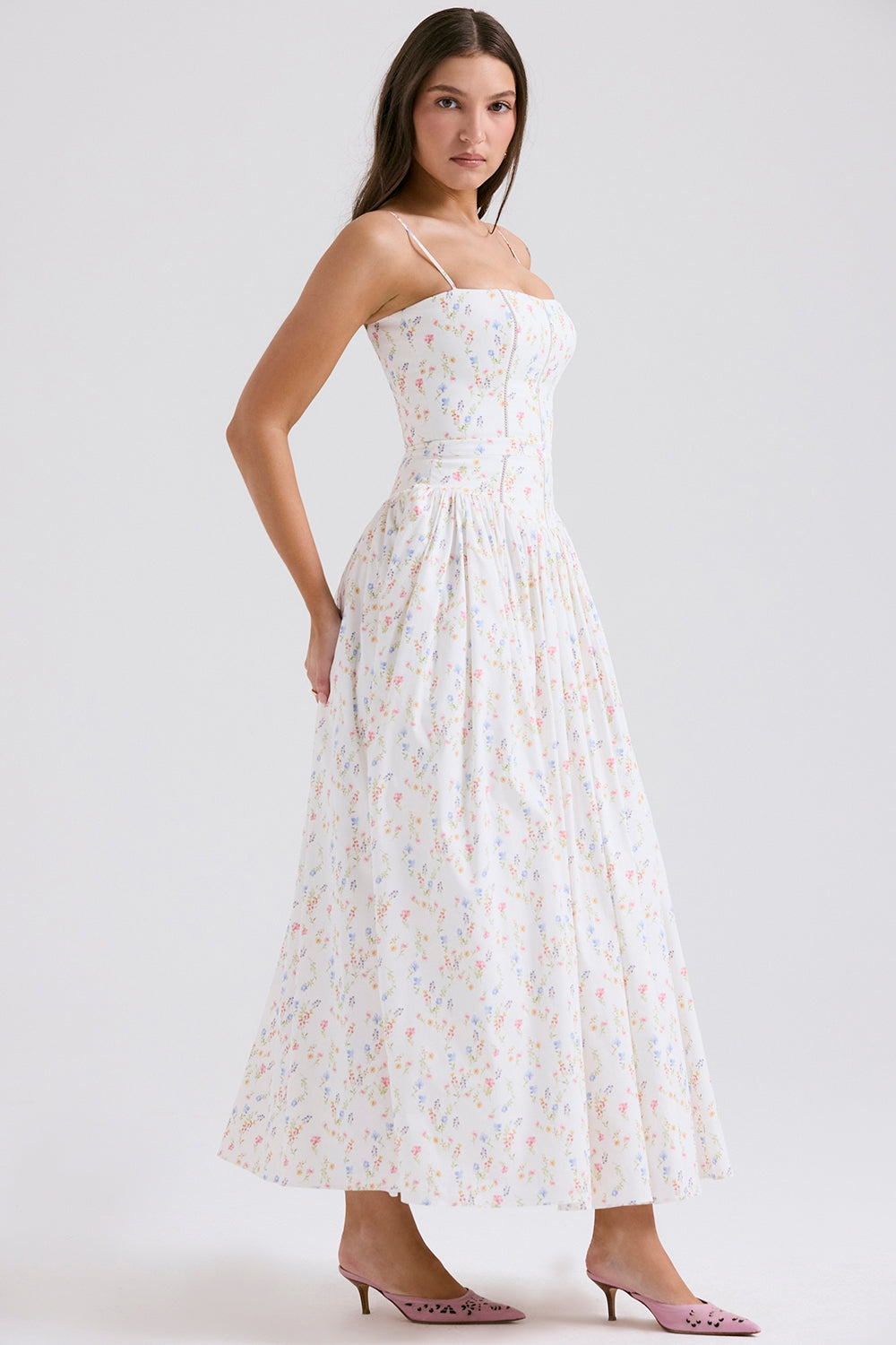 Side profile of the Adeline Corset Midi Dress in white with a delicate multi-color floral pattern, paired with pink kitten heels.