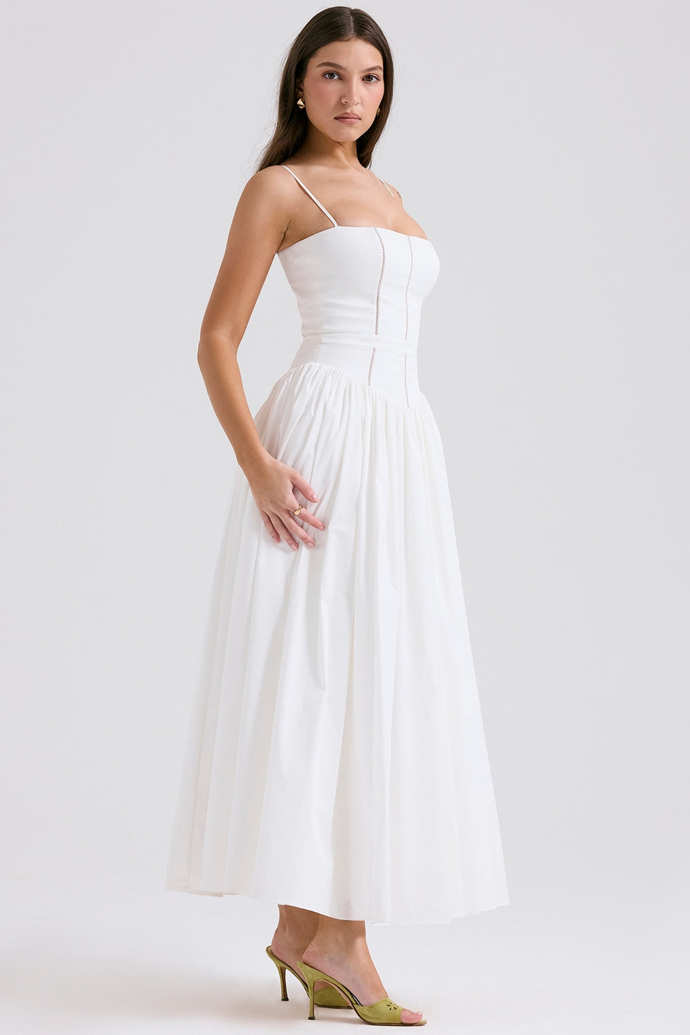 Side view of the solid white Adeline Corset Midi Dress, showcasing the elegant silhouette and tailored fit with green heels.