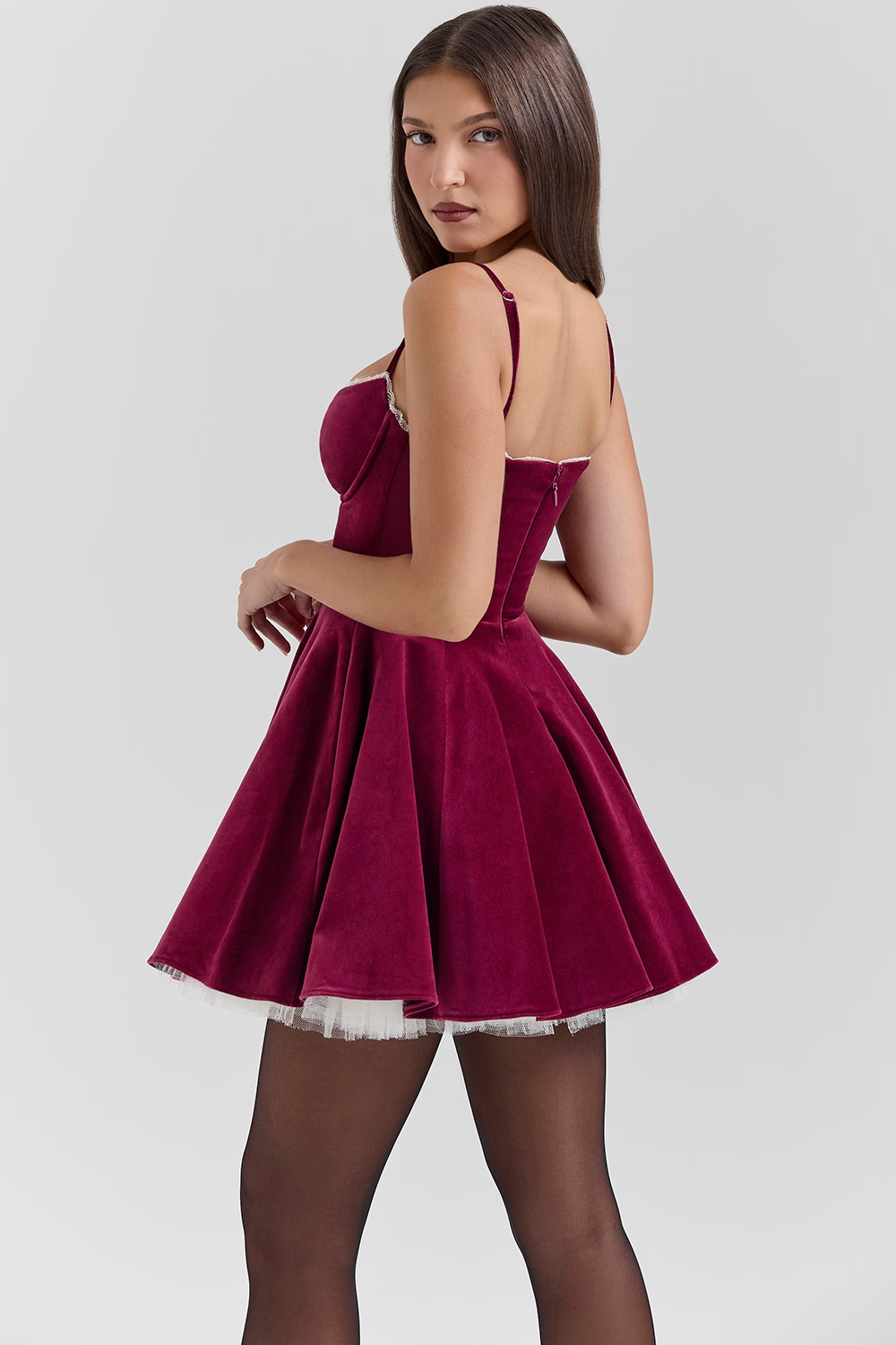 Three-quarter back view of a burgundy velvet mini dress with a full skirt and white lace trim on the bust, worn with black tights.