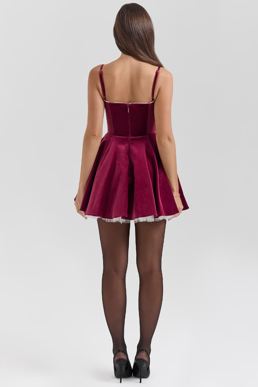 Back view of a burgundy velvet mini dress with a full skirt, white lace trim, and spaghetti straps, worn with black tights.