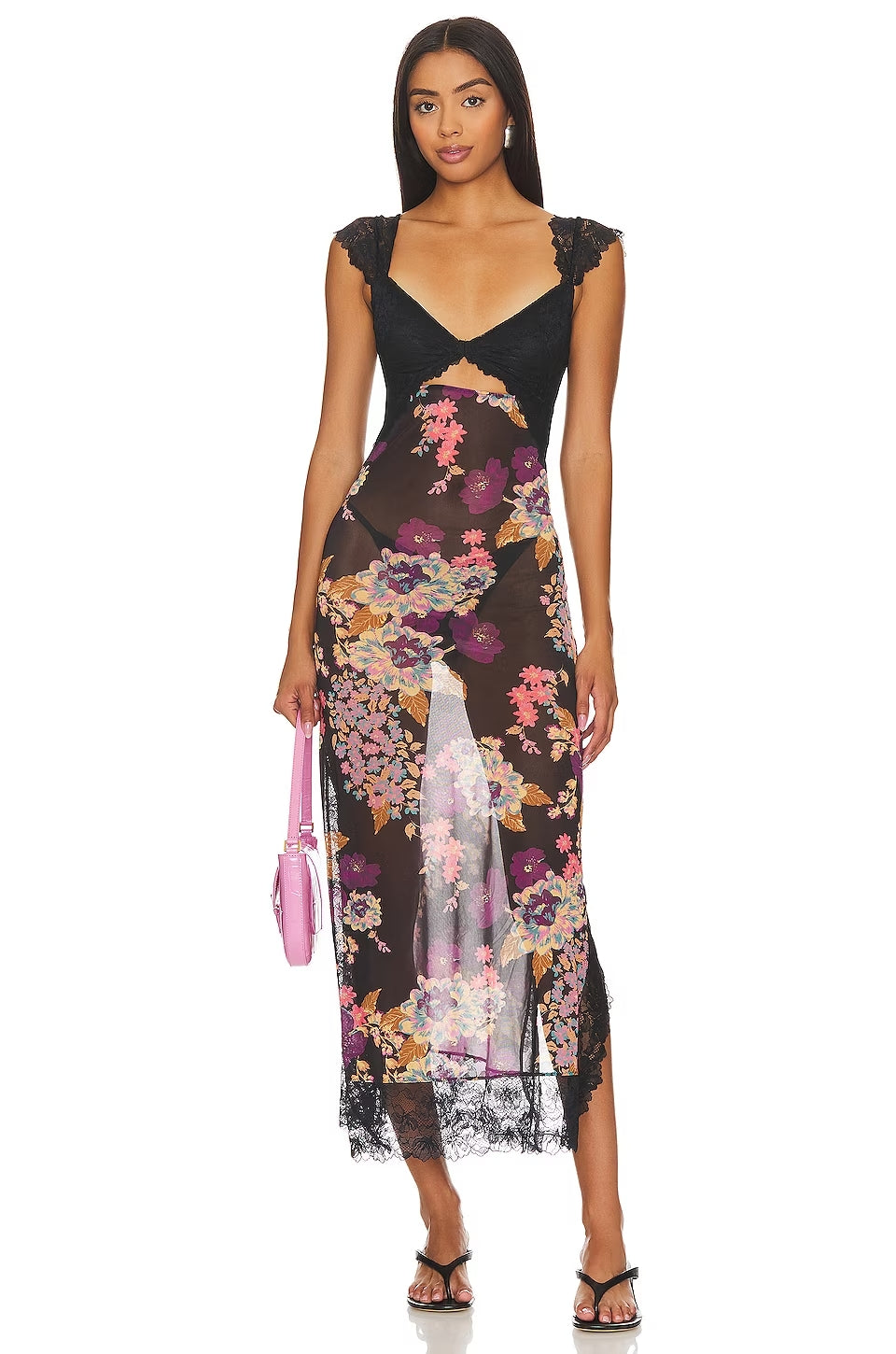 Front view of Aisha backless maxi dress in black with vibrant floral print, lace bust, and cut-out detail, holding a pink handbag.