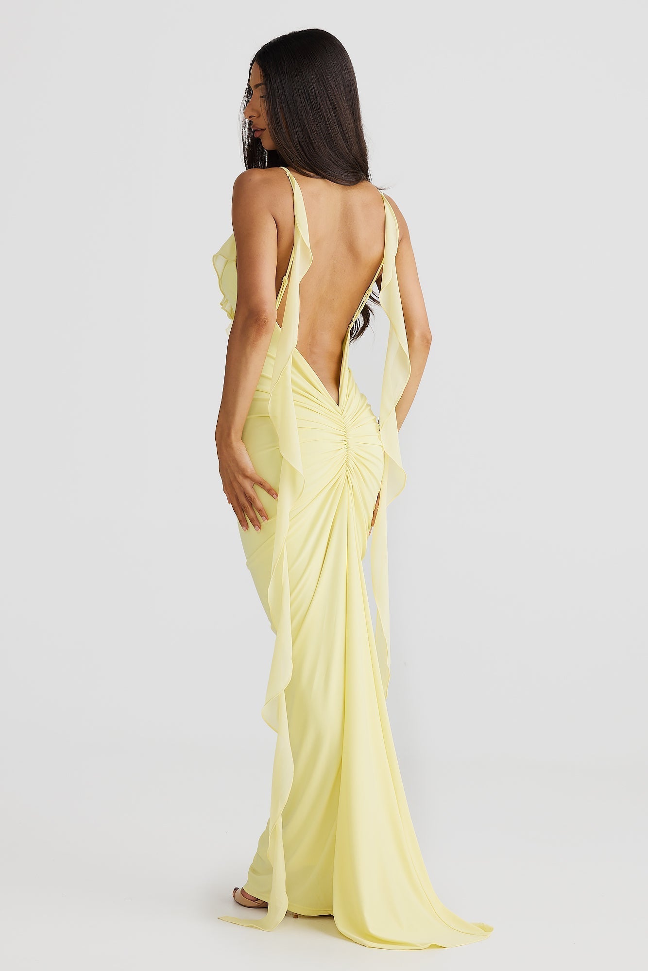 Back view of the light yellow Alexa Ruffle Maxi Dress, featuring an open back design with draped chiffon straps and ruched detailing on the skirt.