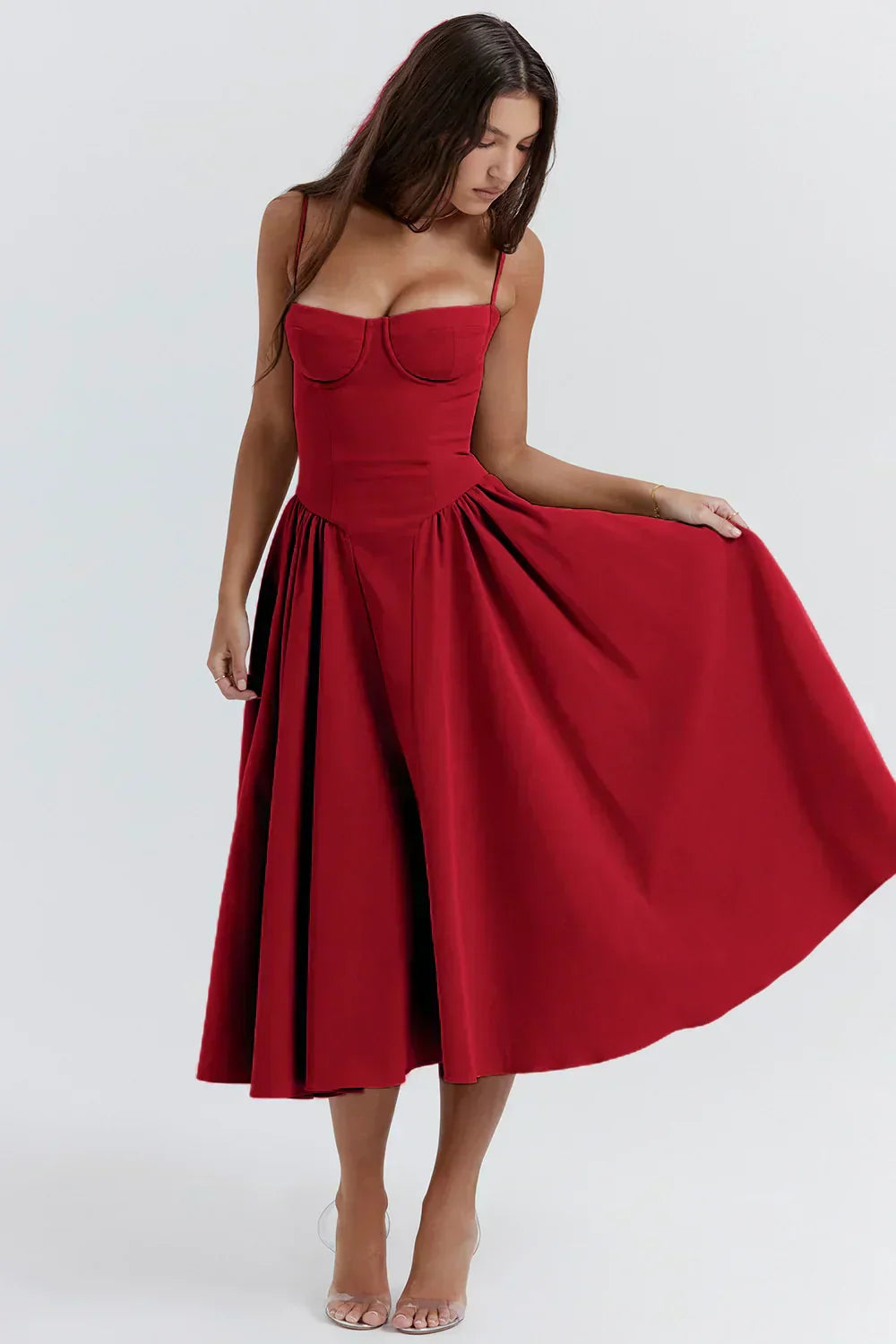 Rich red Alexandra corset midi dress with a sweetheart neckline and a flowing pleated skirt, shown with one hand lifting the skirt.