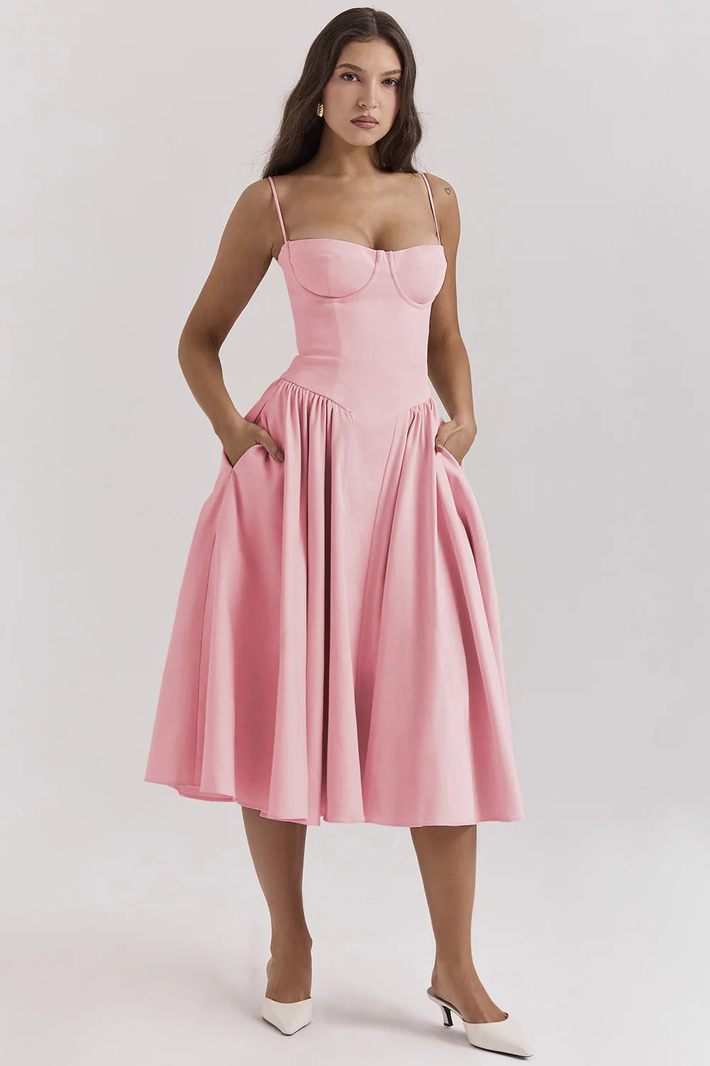 Pink Alexandra corset midi dress with a full pleated skirt and pockets, paired with white heels, offering a modern dress suit look.