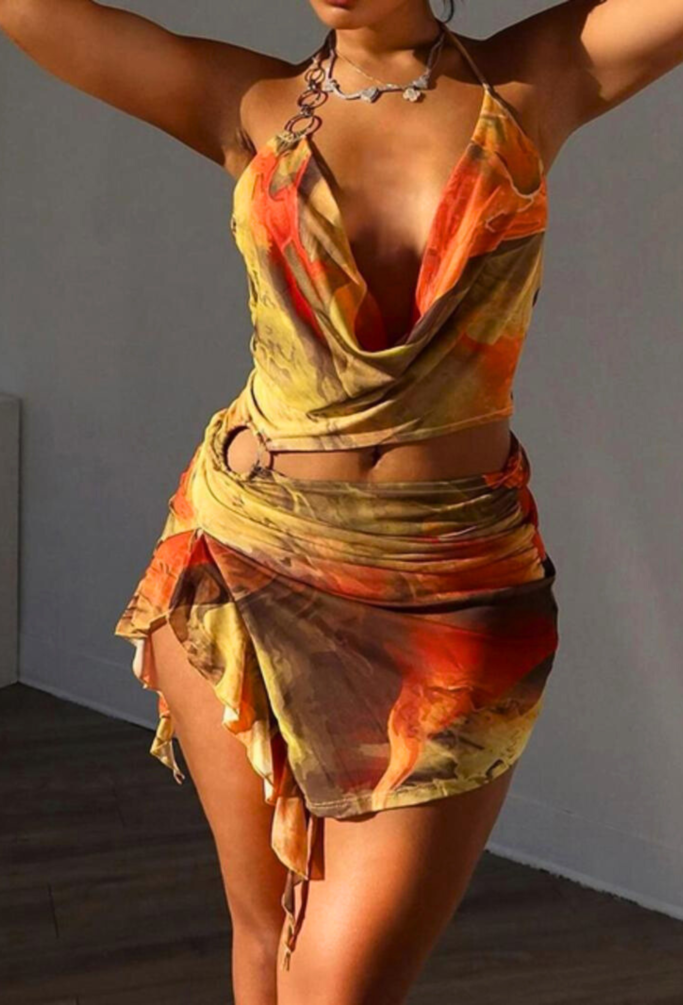 Alexandra Cutout Mini Dress in warm yellow, orange, and brown tones, featuring a deep cowl neck, side cutout, and ruffled mini skirt.