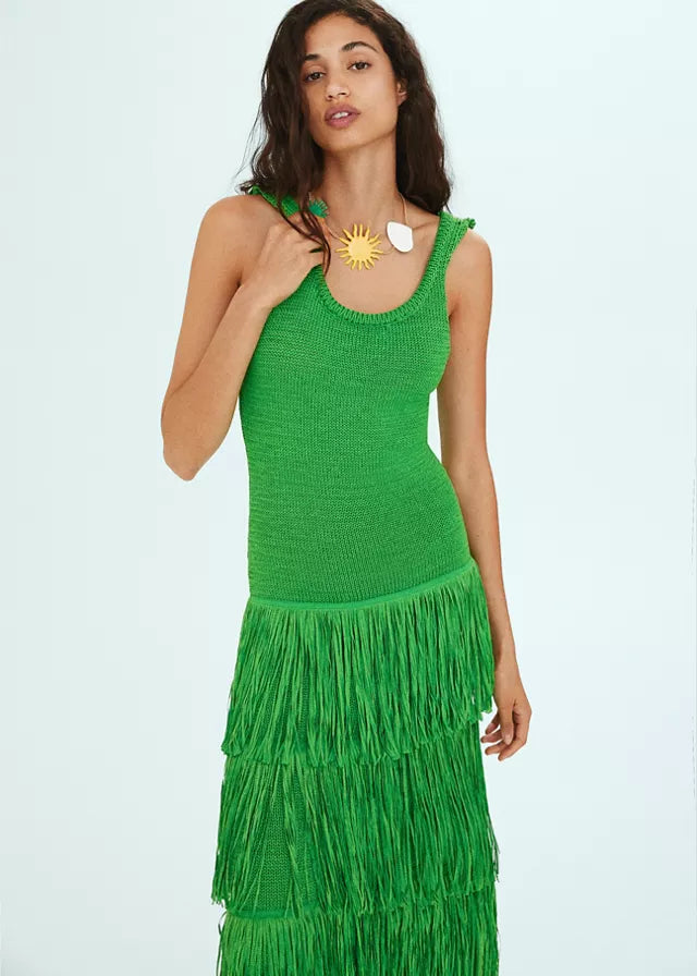 Bright green knit midi dress with tiered fringe skirt and scoop neck, paired with a sun pendant necklace.