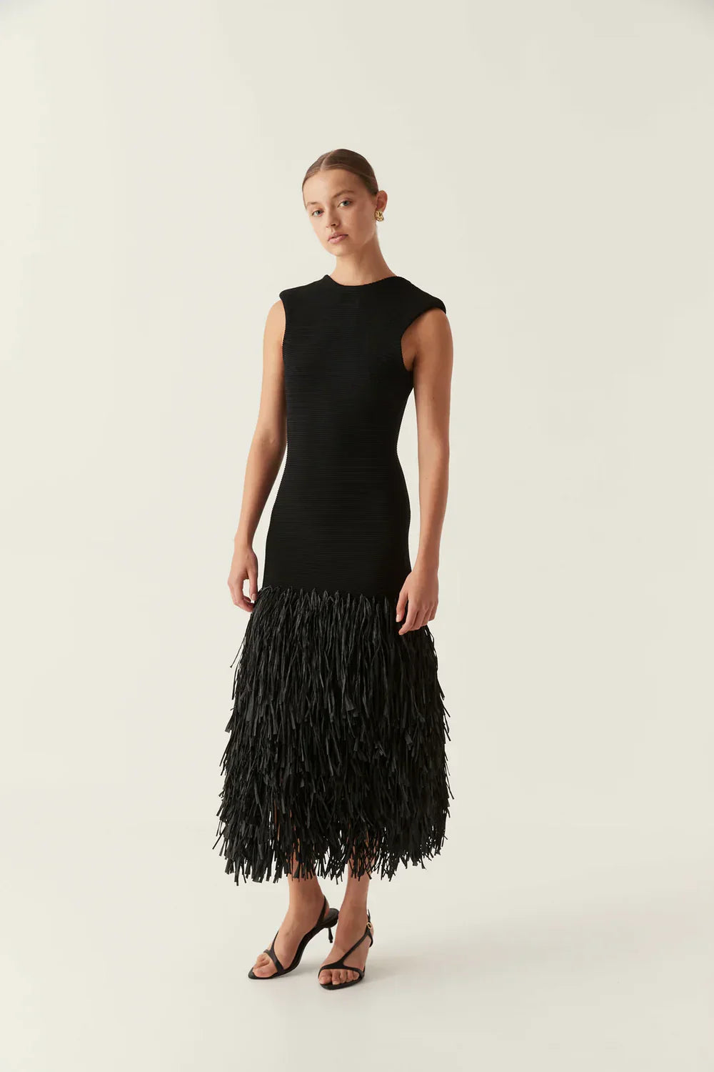 Full length view of a black ribbed midi dress featuring a sleeveless design and a full fringe skirt.