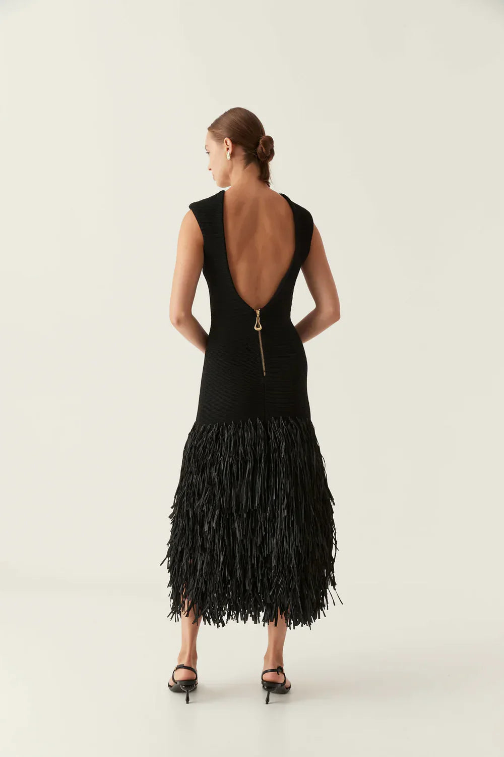 Back view of the black midi dress, showing a deep scoop back and a visible gold zipper detail above the fringe skirt.