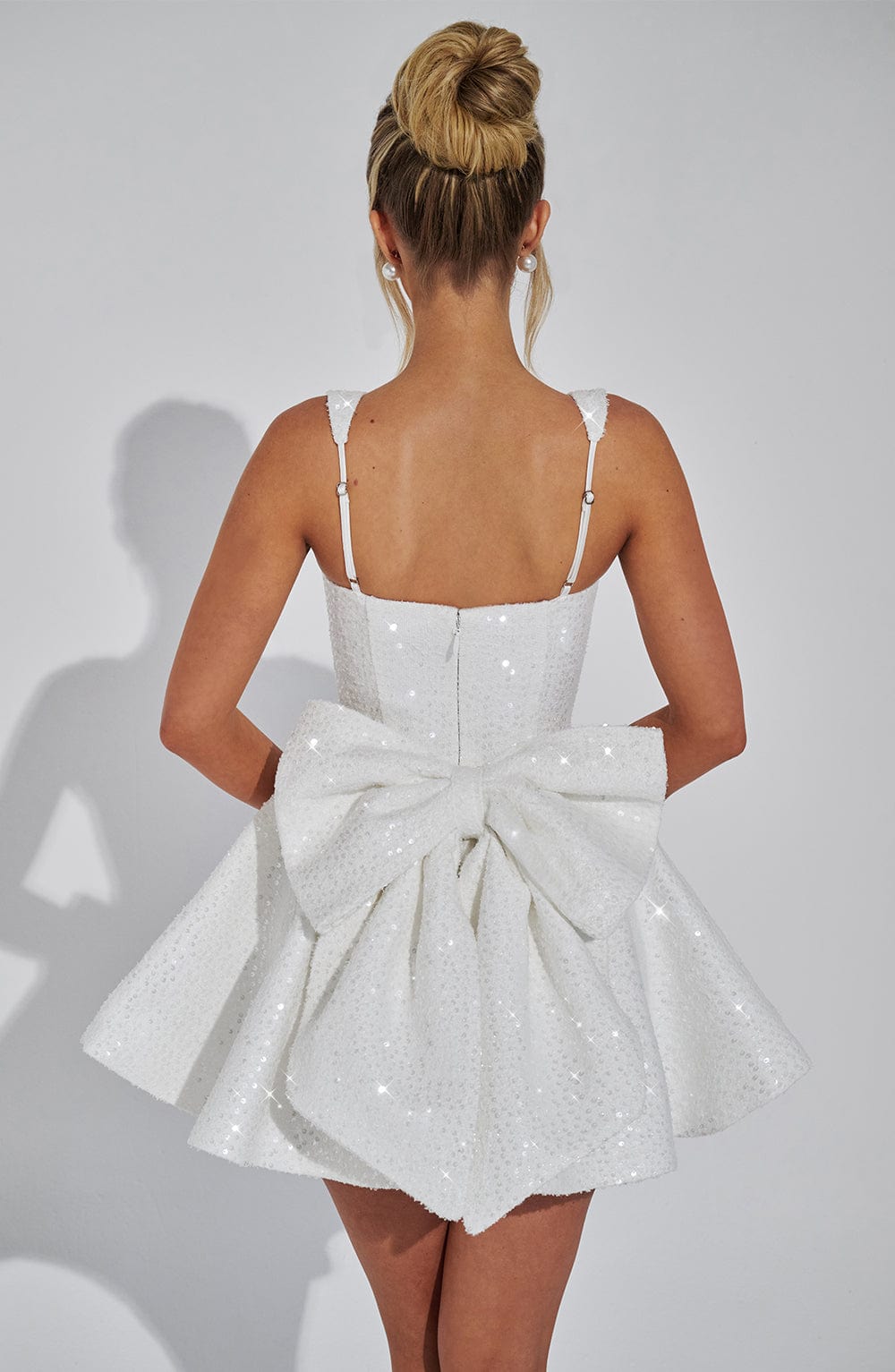 Rear view of a white sequin mini dress with a large, structured bow detail and delicate adjustable straps, a chic wedding suit dress.