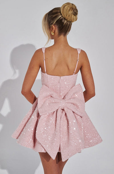 Back view of a pink sequin mini dress with a prominent, oversized bow and thin adjustable straps, a playful suit dress.