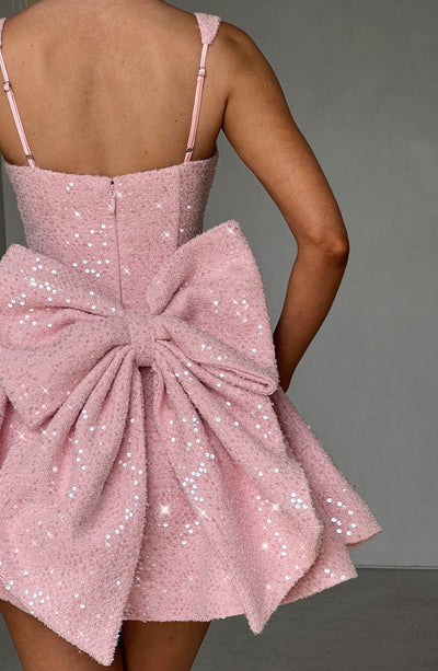 Close-up back view of the pink sequin mini dress, highlighting the texture of the fabric and the large, ruffled bow detail.