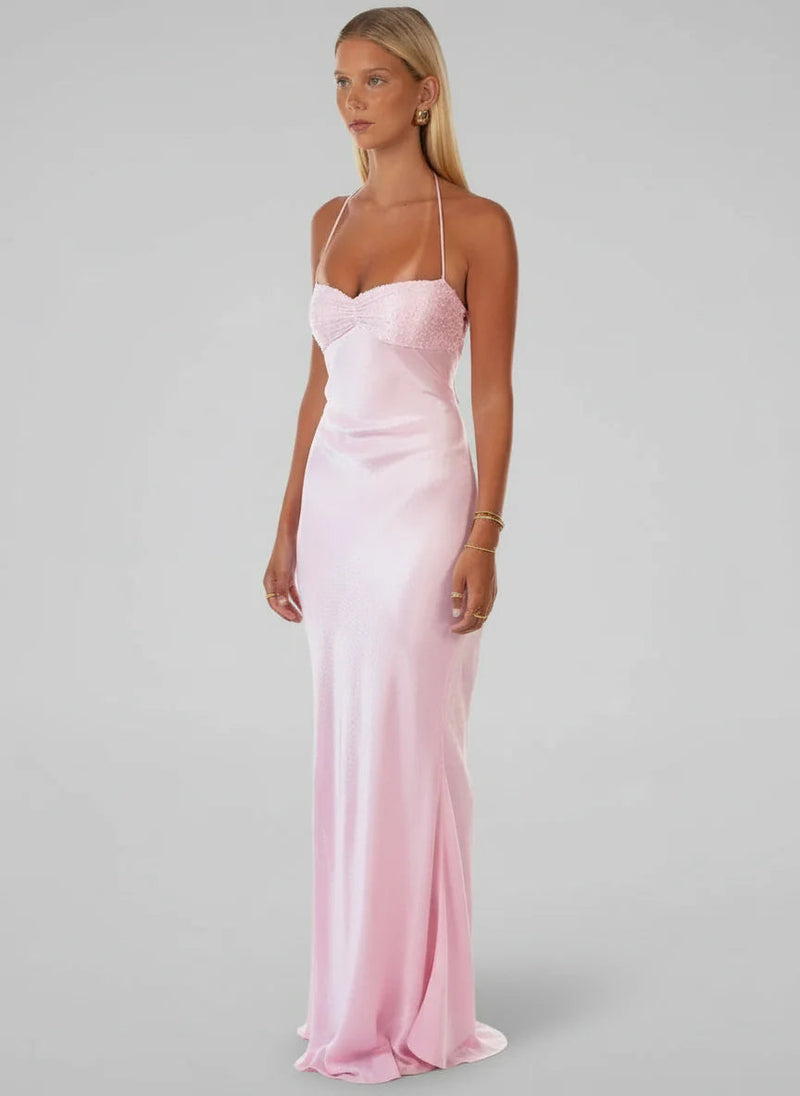 Side profile of a woman wearing a flowing light pink satin halter maxi dress with delicate beaded detailing on the bodice.