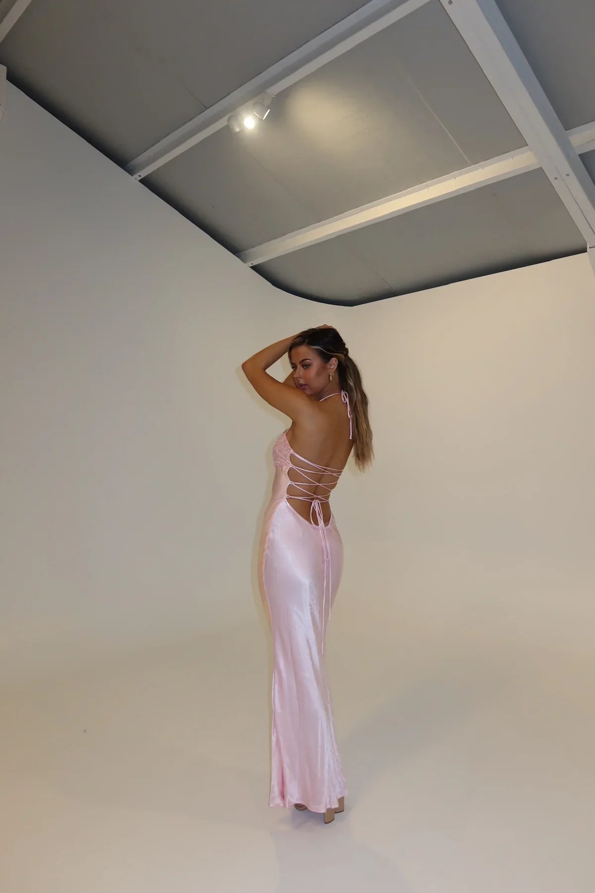 Back view of the light pink Amaya lace halter maxi dress on a model, showing the detailed criss-cross back straps.