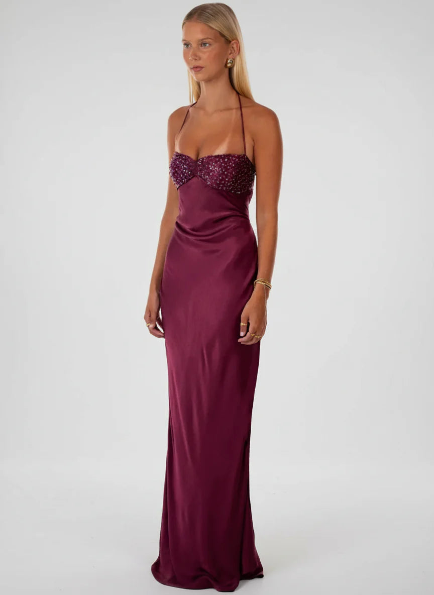 Side profile of a woman in a deep burgundy satin halter maxi dress, highlighting the luxurious fabric and beaded top.