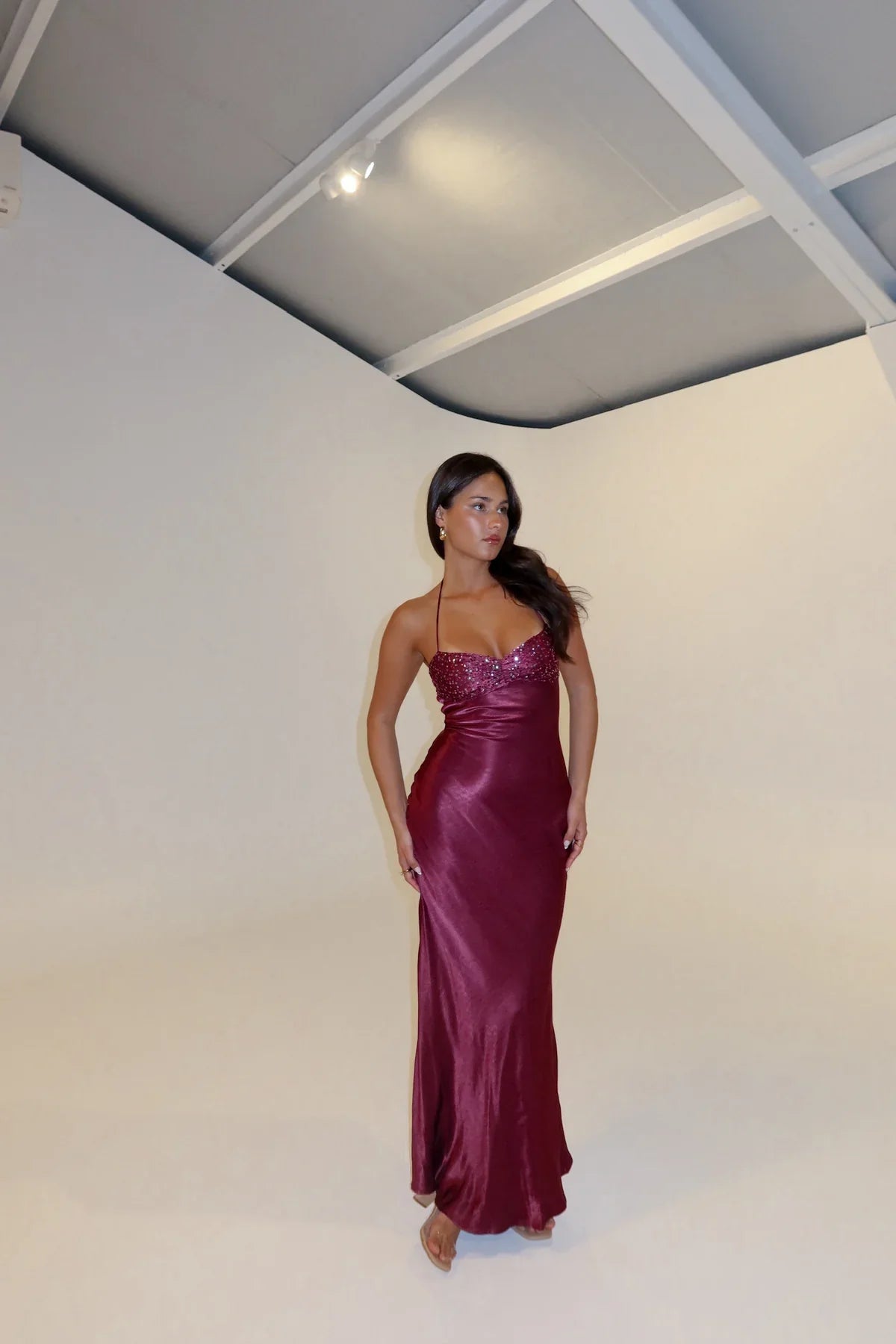 Model posing in a deep burgundy Amaya lace halter maxi dress, showcasing the flattering fit and beaded bodice.