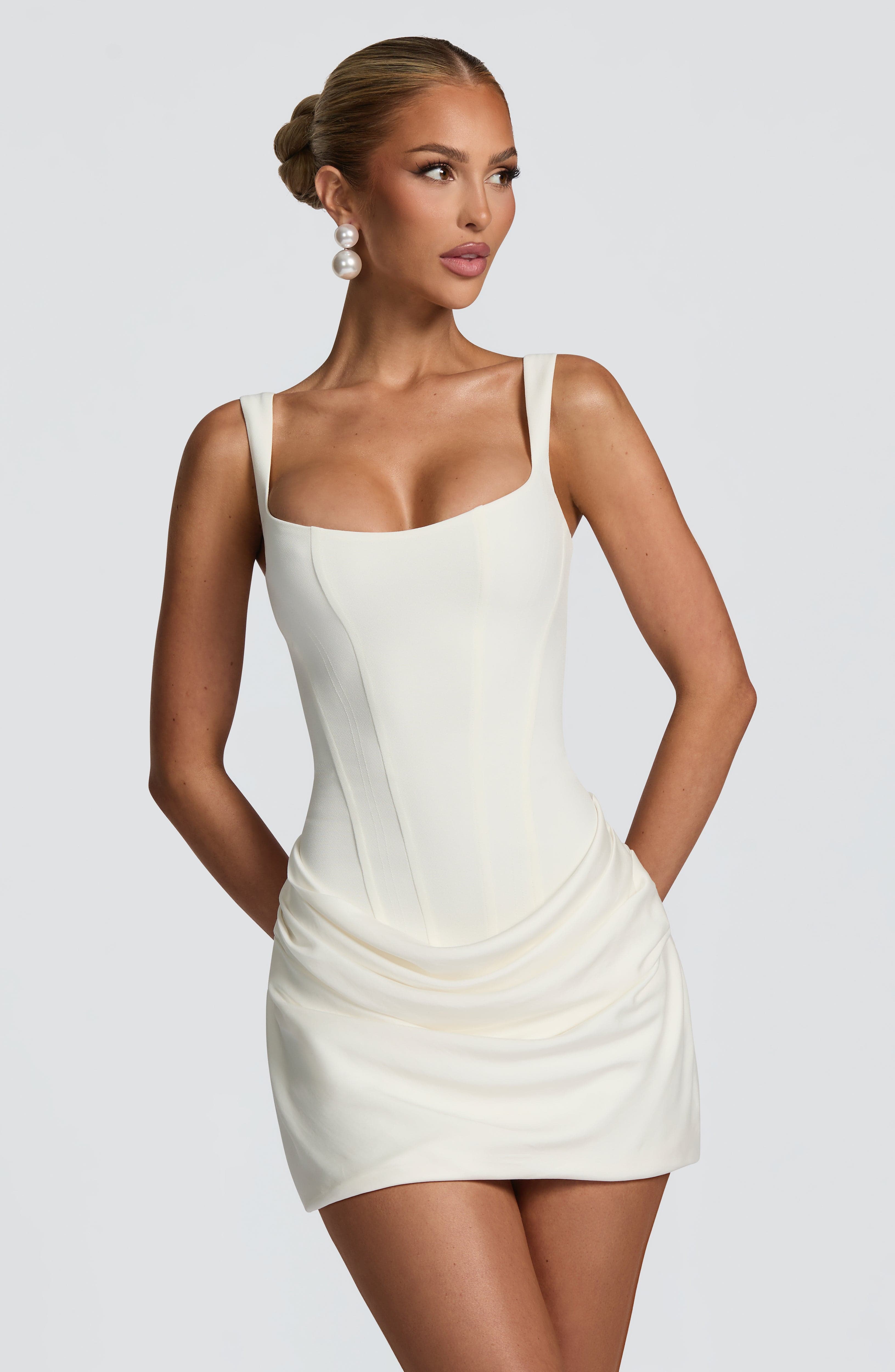 Upper body view of a woman wearing an ivory Amelie Ruched Mini Dress with a structured bodice and ruched skirt.