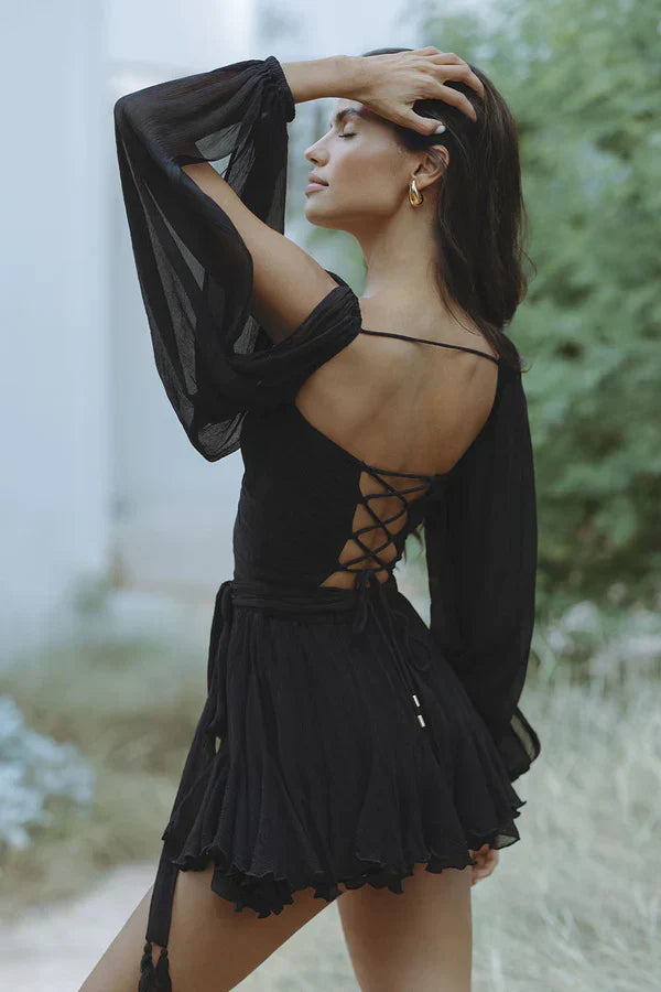 Side profile of the black Amira Draped Mini Dress, showing the open back with crisscross lacing and flowing sleeves.