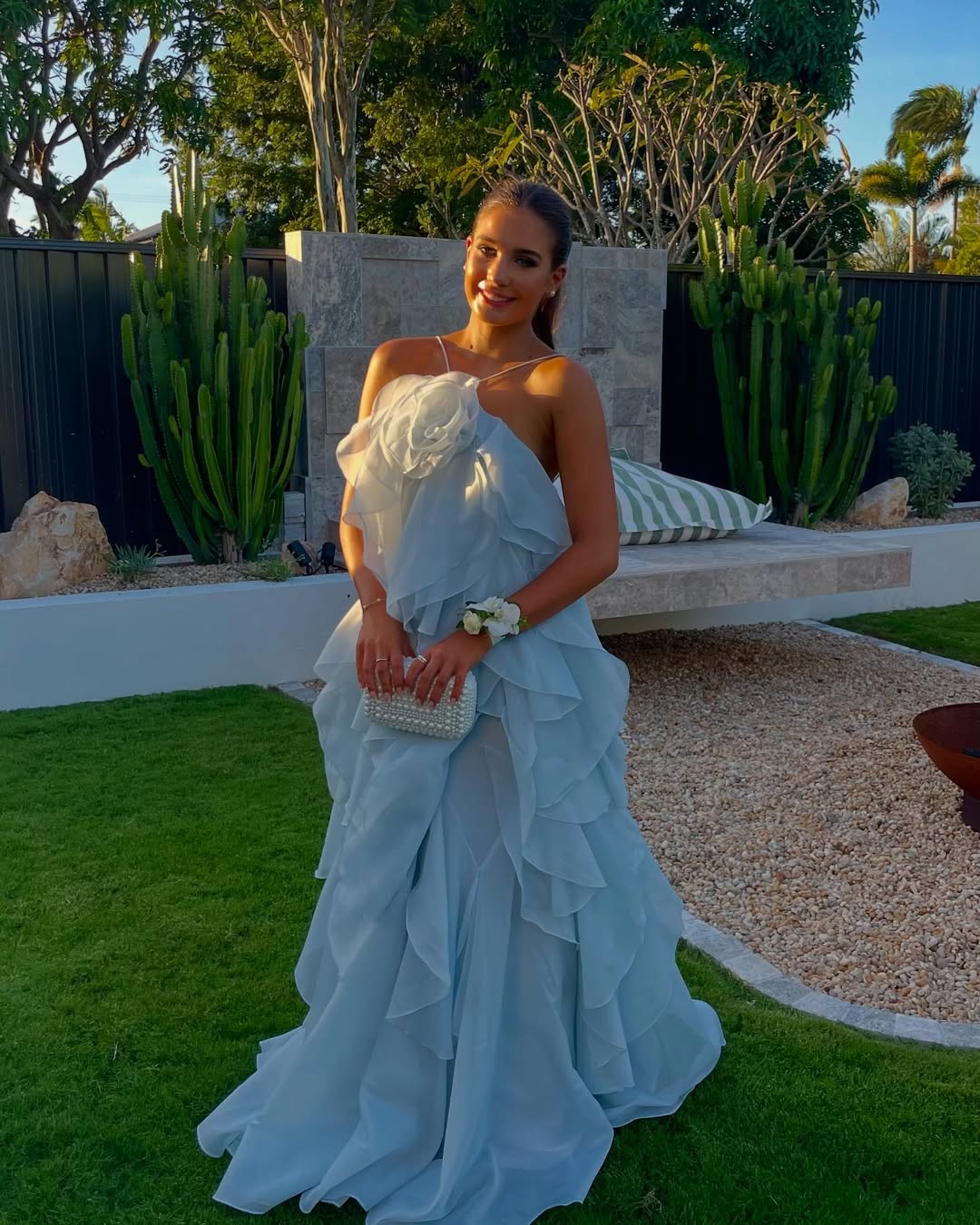 Front view of an Andrea Ruffle Maxi Dress in light blue, featuring a white floral bust and pearl clutch.