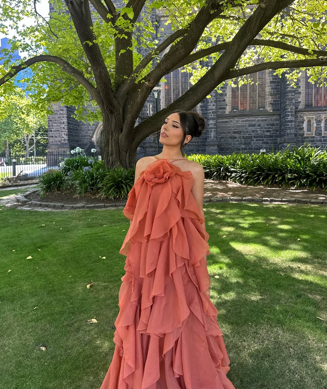 Front view of an Andrea Ruffle Maxi Dress in a vibrant peach color with a large floral detail on the bust.