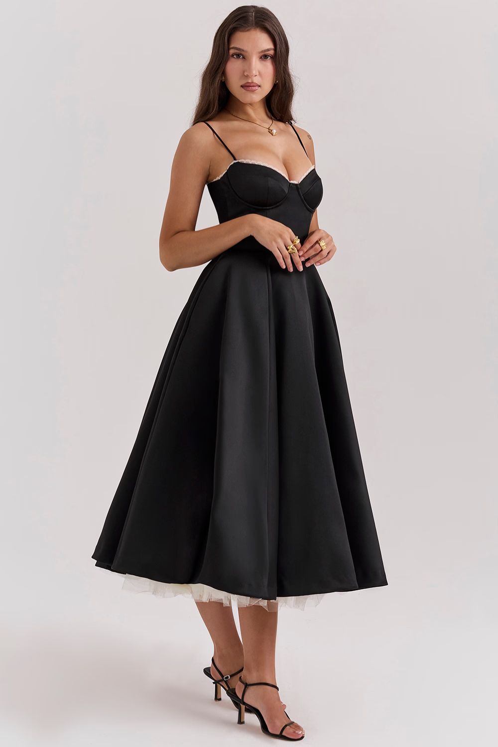 Front view of a woman in a black Angela corset midi dress with a sweetheart neckline and a full skirt, showing a hint of a cream tulle underskirt.