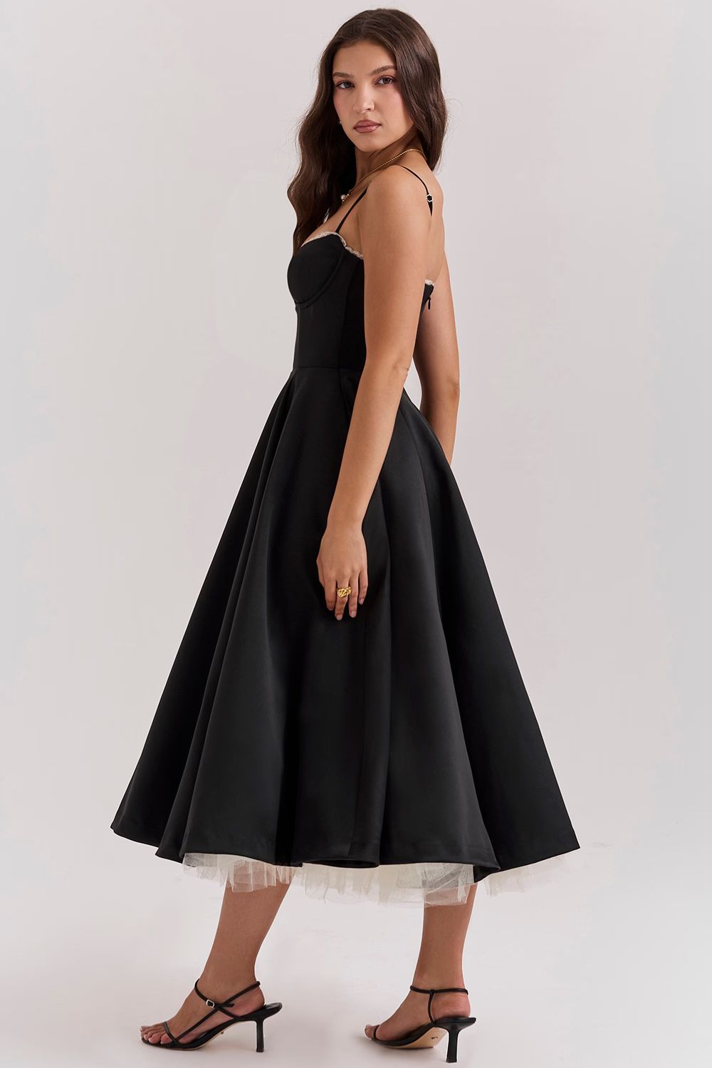 Side profile of a woman wearing a black Angela corset midi dress, showcasing the voluminous skirt and delicate spaghetti straps.
