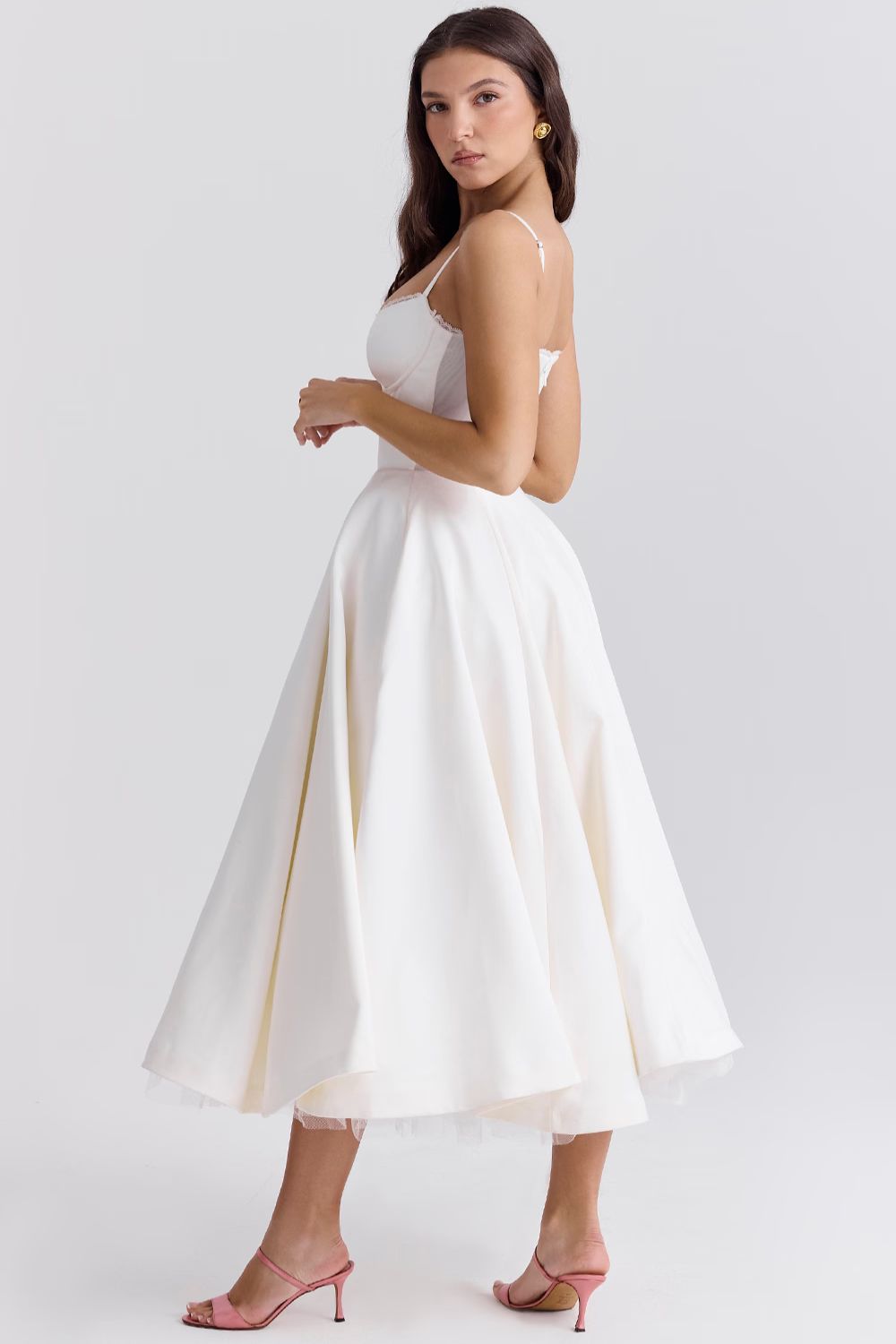 Side view of a woman wearing a white Angela corset midi dress, highlighting the elegant silhouette and the flow of the skirt.