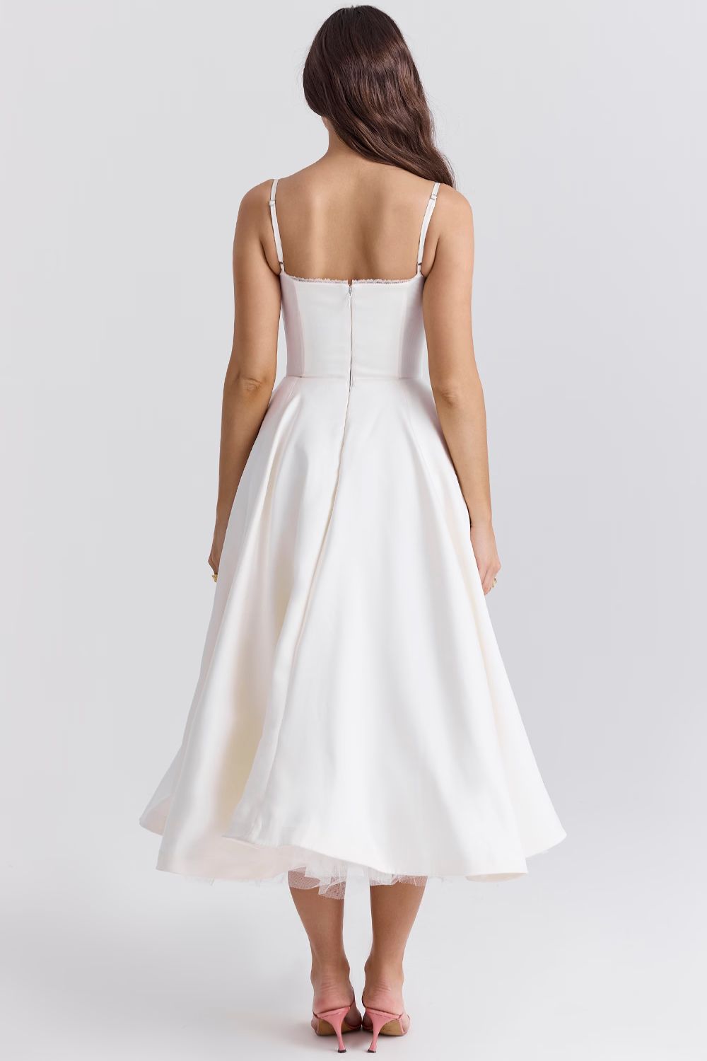 Back view of a woman in a white Angela corset midi dress, showing the delicate spaghetti straps and the zip closure.