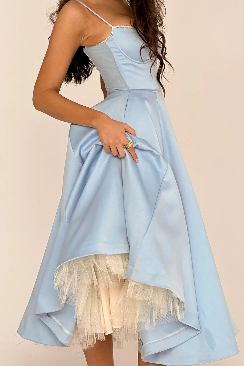 Light blue corset midi dress with a full skirt, showing white tulle peeking from the hem and a gold ring on her finger.