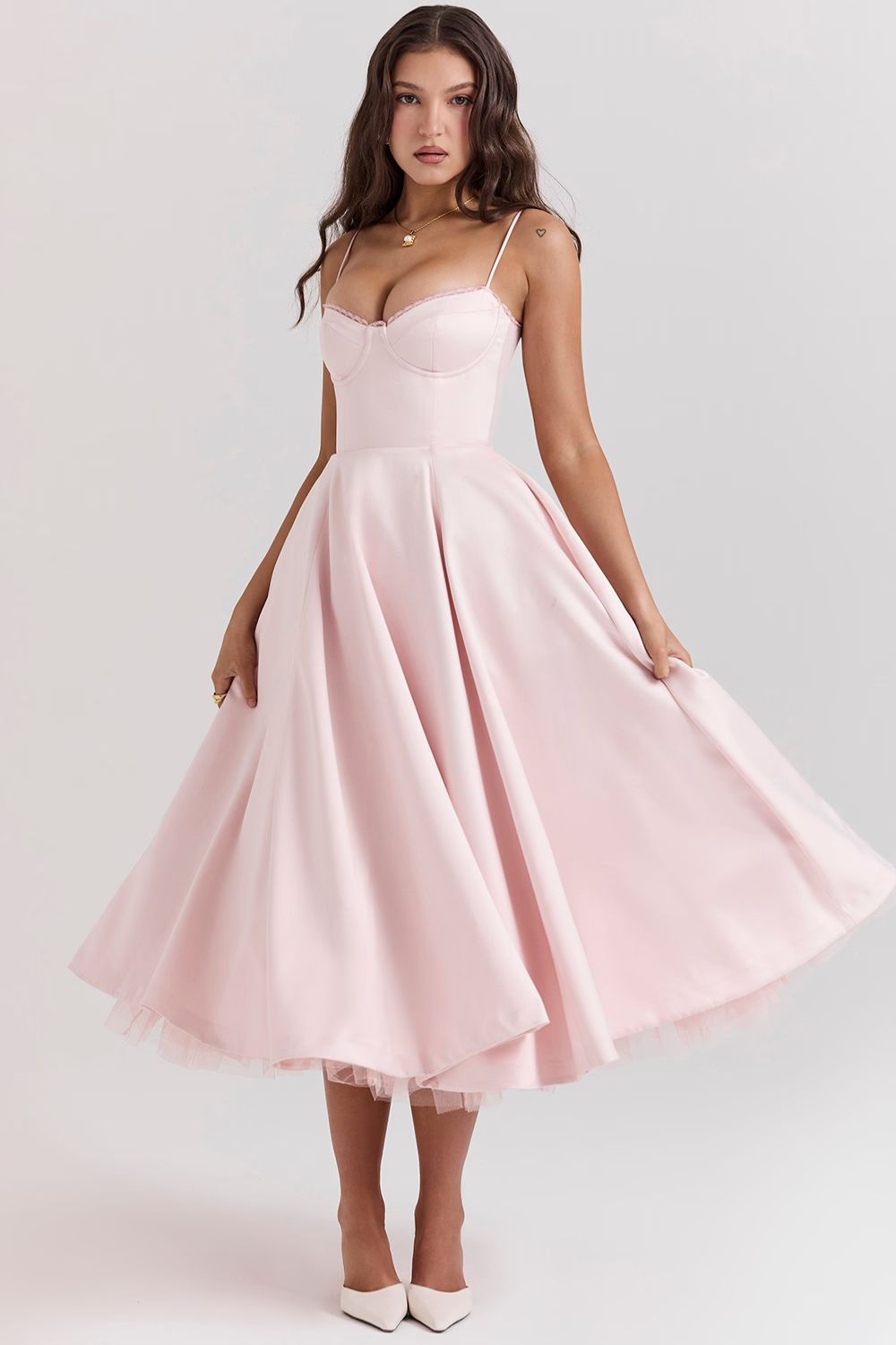 Model wearing a light pink corset midi dress with a full, flowing skirt, paired with white designer shoes.