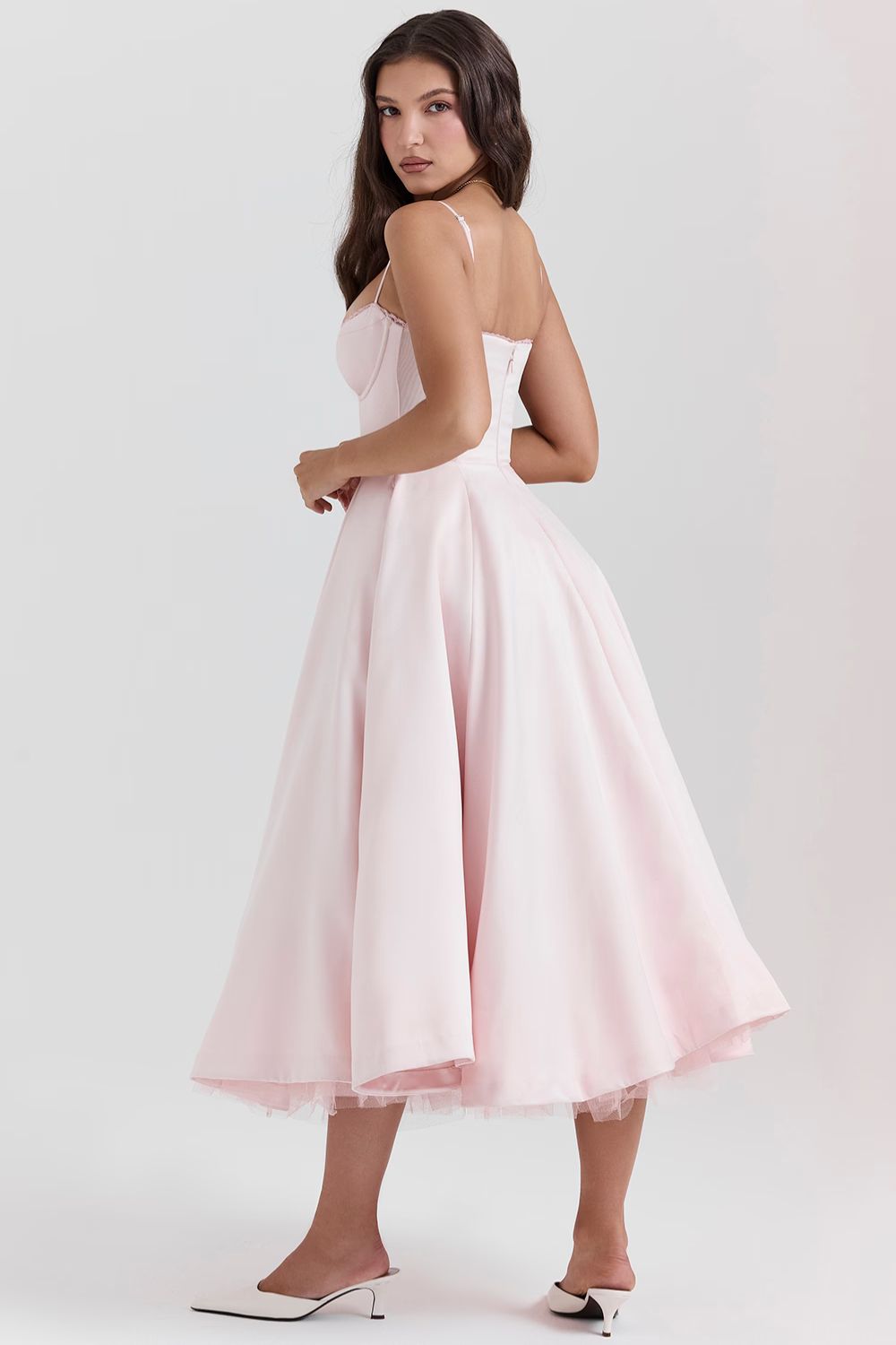 Side view of a model in a light pink corset midi dress, highlighting the swing of the skirt and subtle tulle lining.