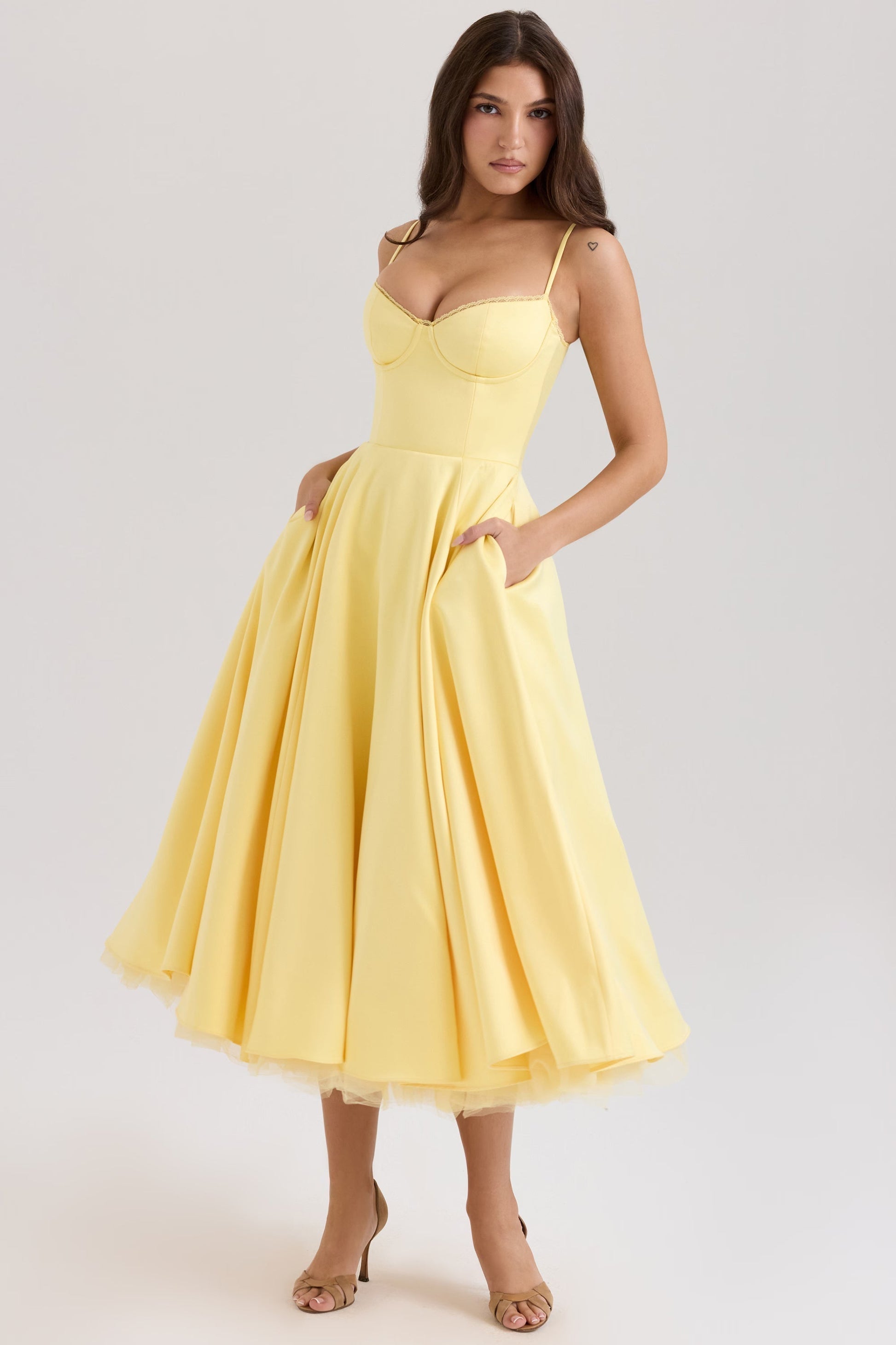 Model in a bright yellow Angela corset midi dress with a full skirt and pockets, paired with brown heels.