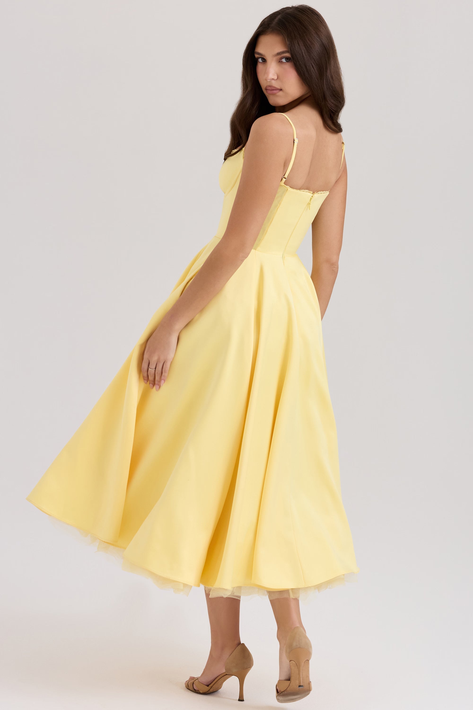 Back view of a model in a bright yellow Angela corset midi dress, showcasing the flowing skirt and brown heels.