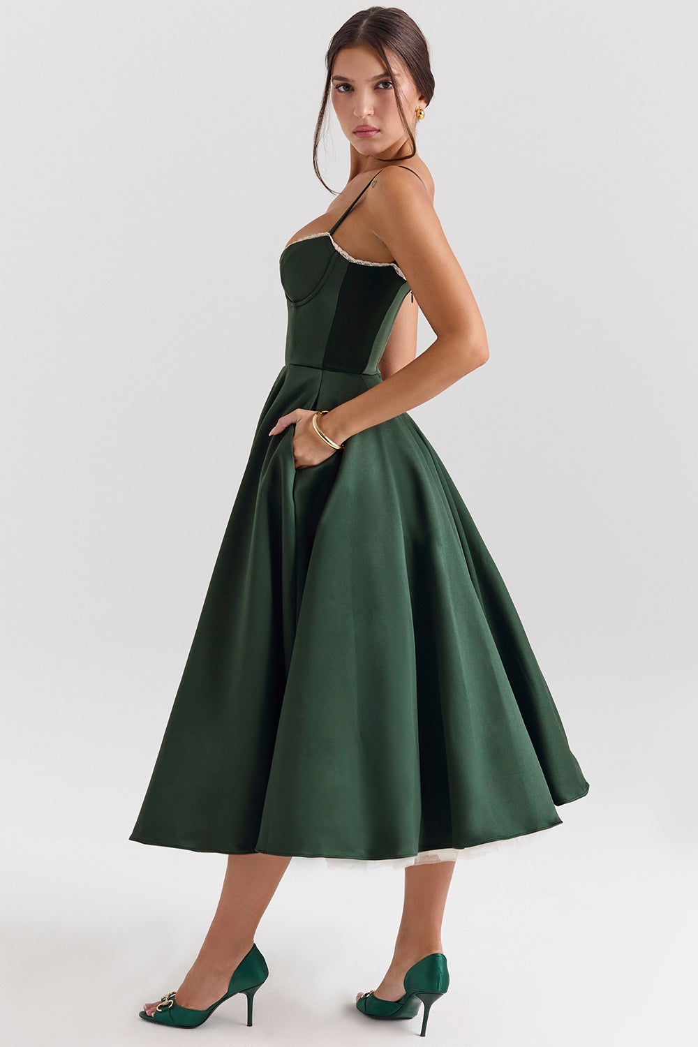 Side view of a dark green Angela Corset Midi Dress, highlighting the full skirt, pockets, and white lace trim on the bust.
