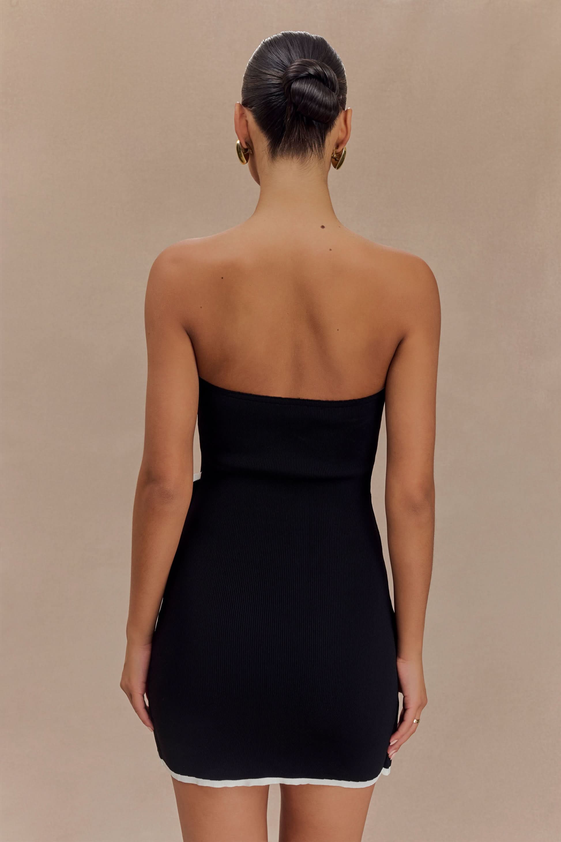 Back view of a woman in a black strapless mini dress with white contrasting trim.