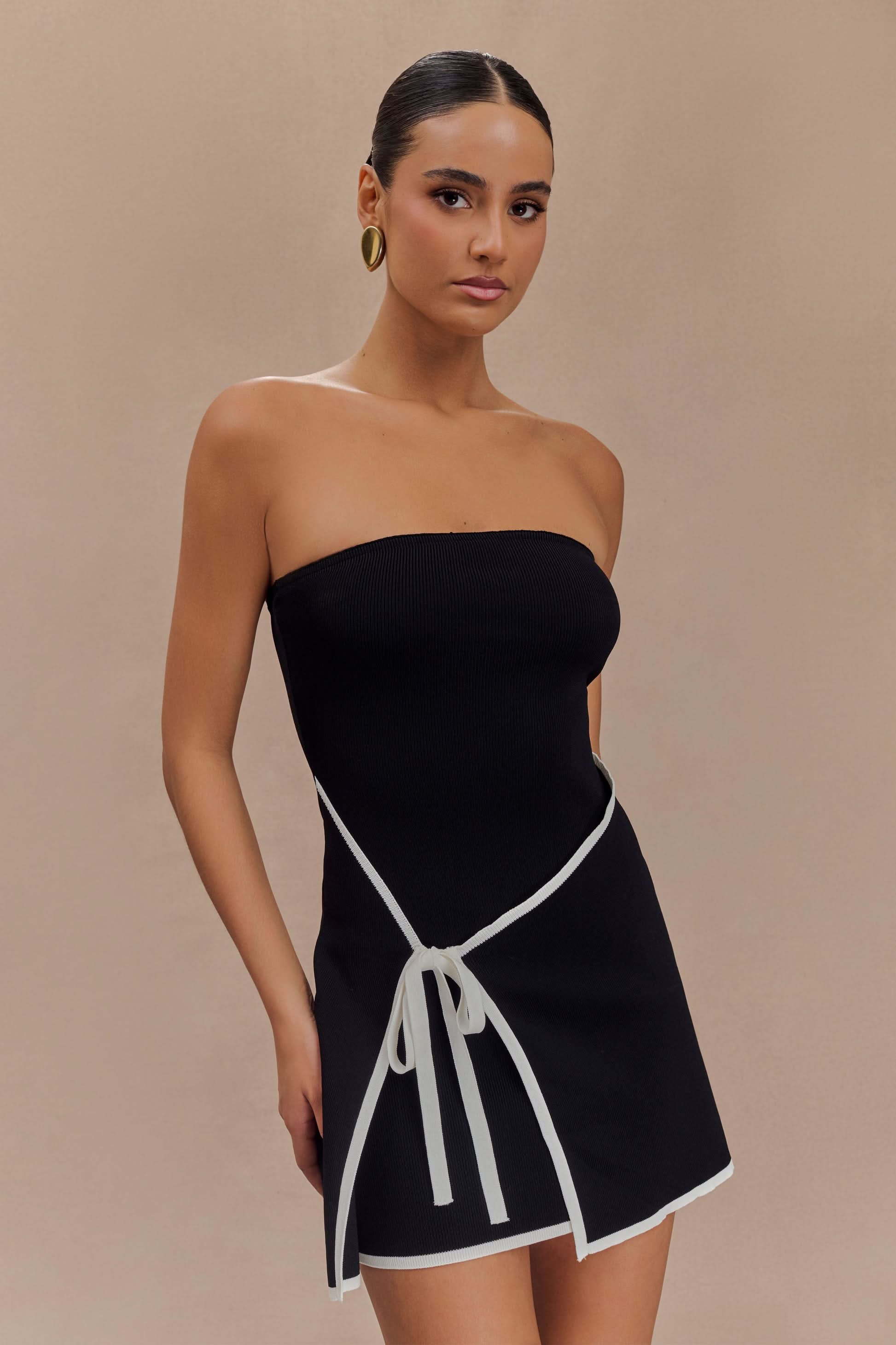 Front oblique view of a woman in a black strapless mini dress with white wrap tie detail for women.