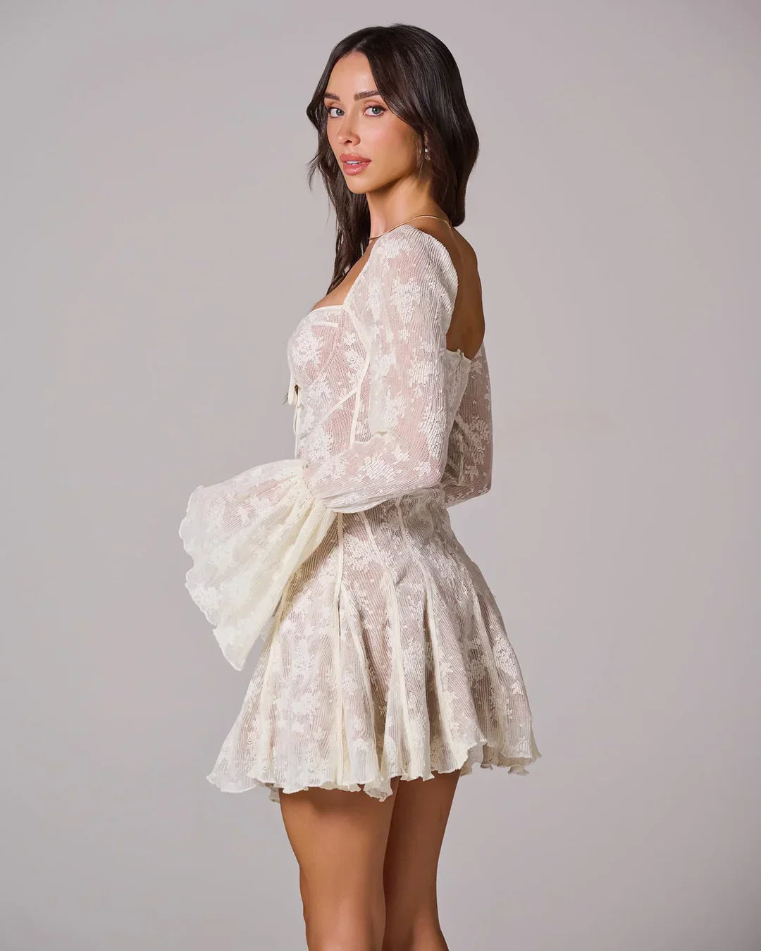 Close-up back view of a white lace mini dress, showcasing the textured fabric and pleated skirt detail.