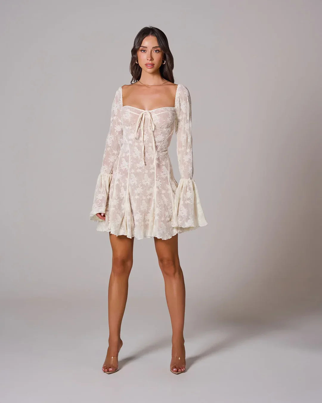 Full front view of a cream white lace mini dress, featuring a square neckline, long bell sleeves, and a delicate lace pattern throughout.