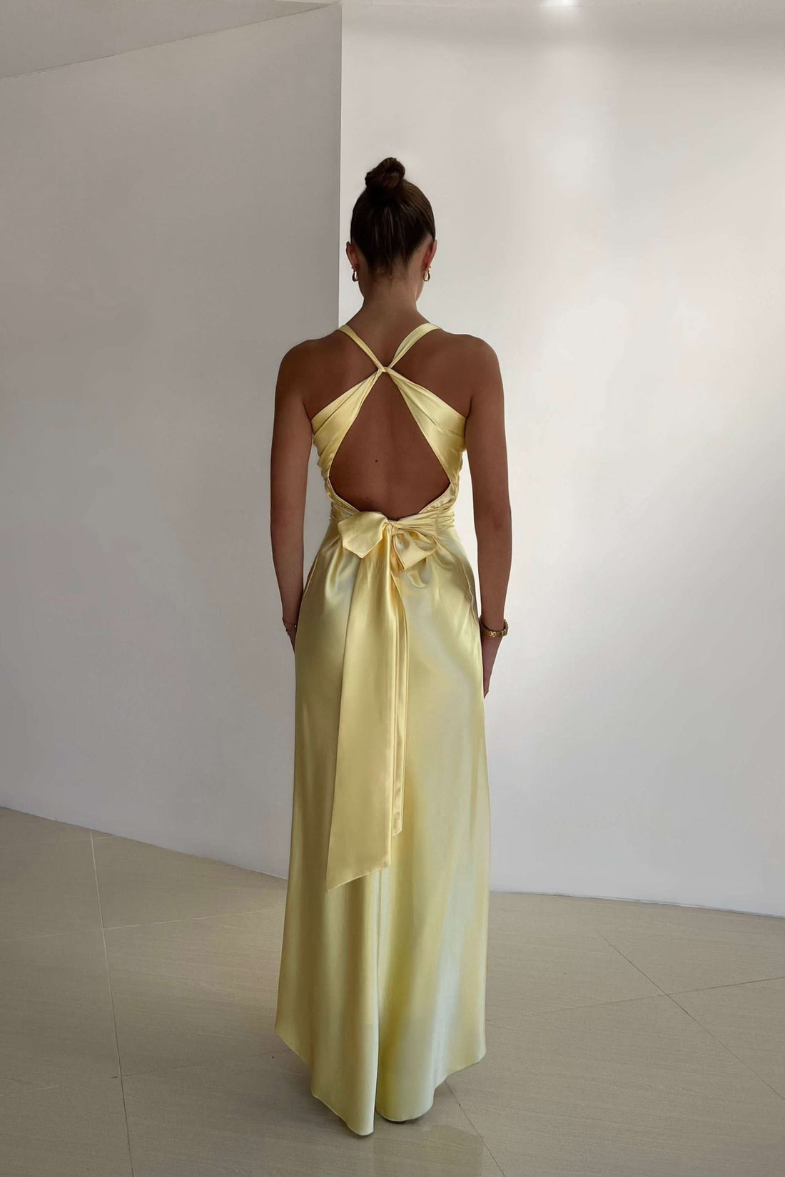 Full-length yellow satin maxi dress with a twisted halter neckline and open back design, perfect for special occasions.