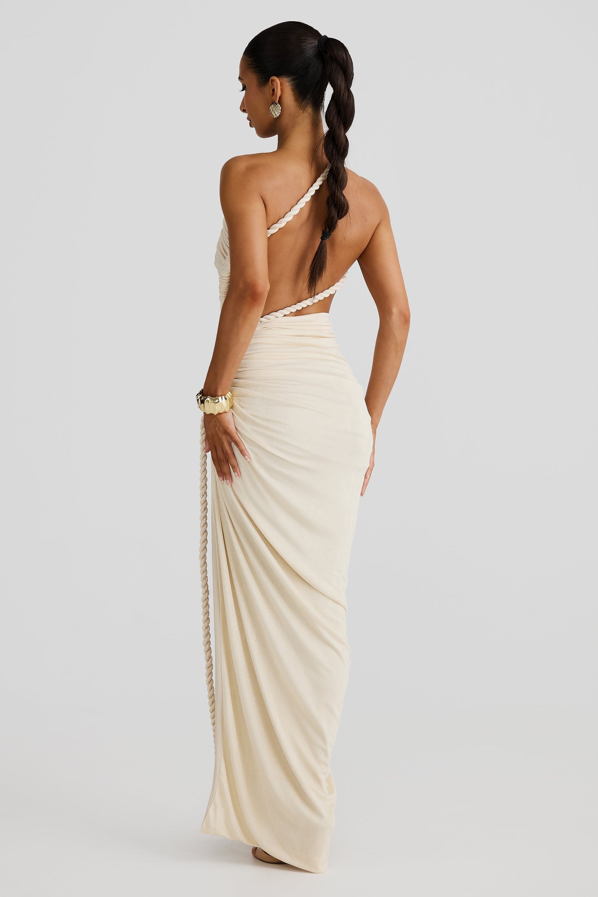 Back view of the cream Aspen Rope Maxi Dress, showing the open back design with a single rope strap and flowing skirt.