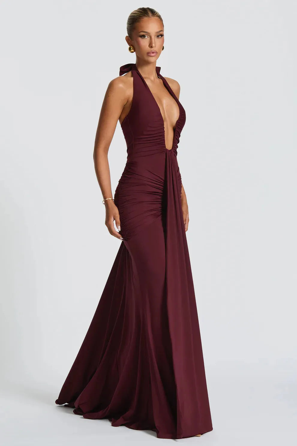 Side view of a burgundy ruched maxi dress, highlighting the halter neckline and the elegant drape of the skirt.