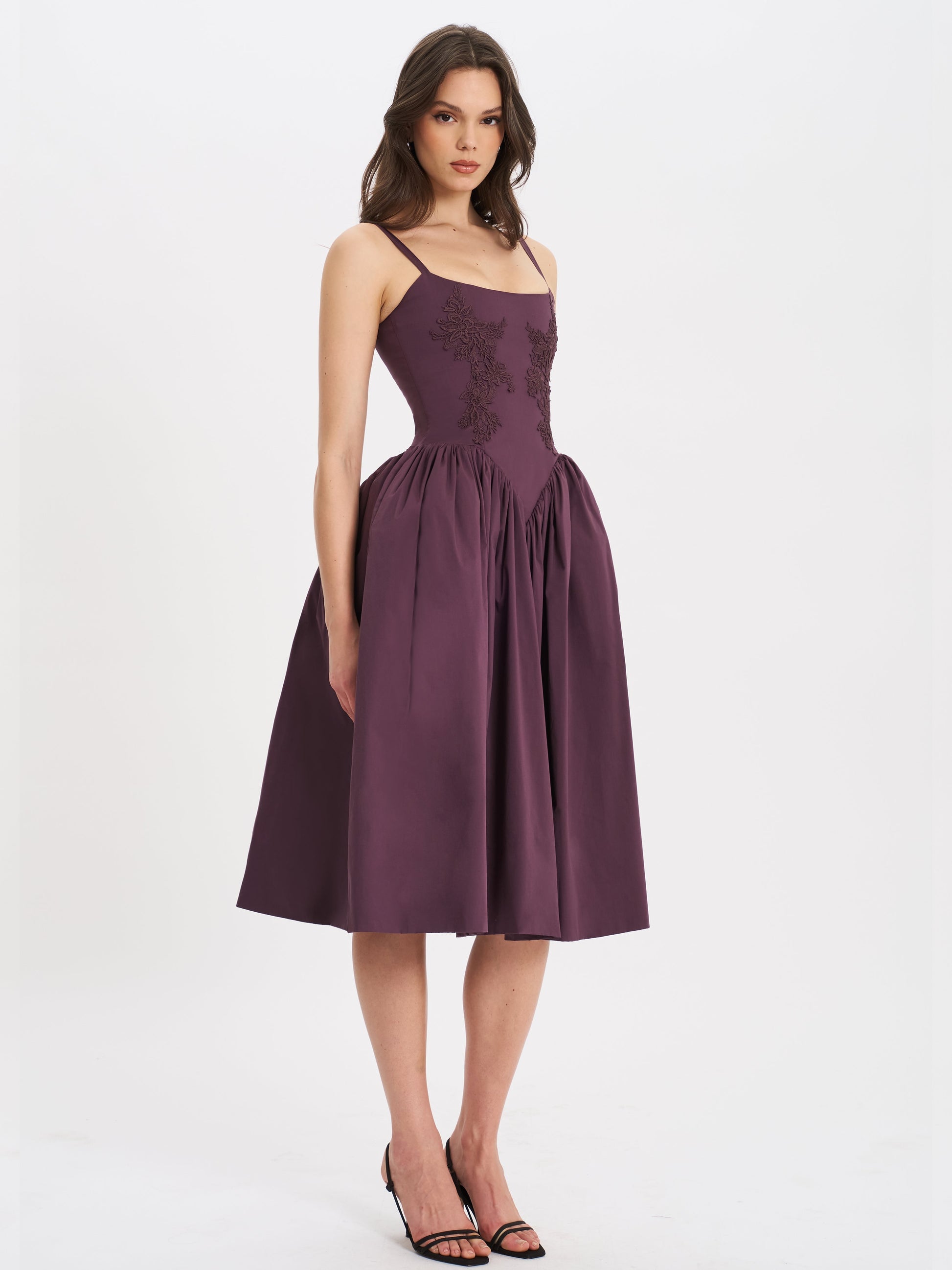 Side profile of woman wearing purple embroidered midi dress with elegant full skirt.