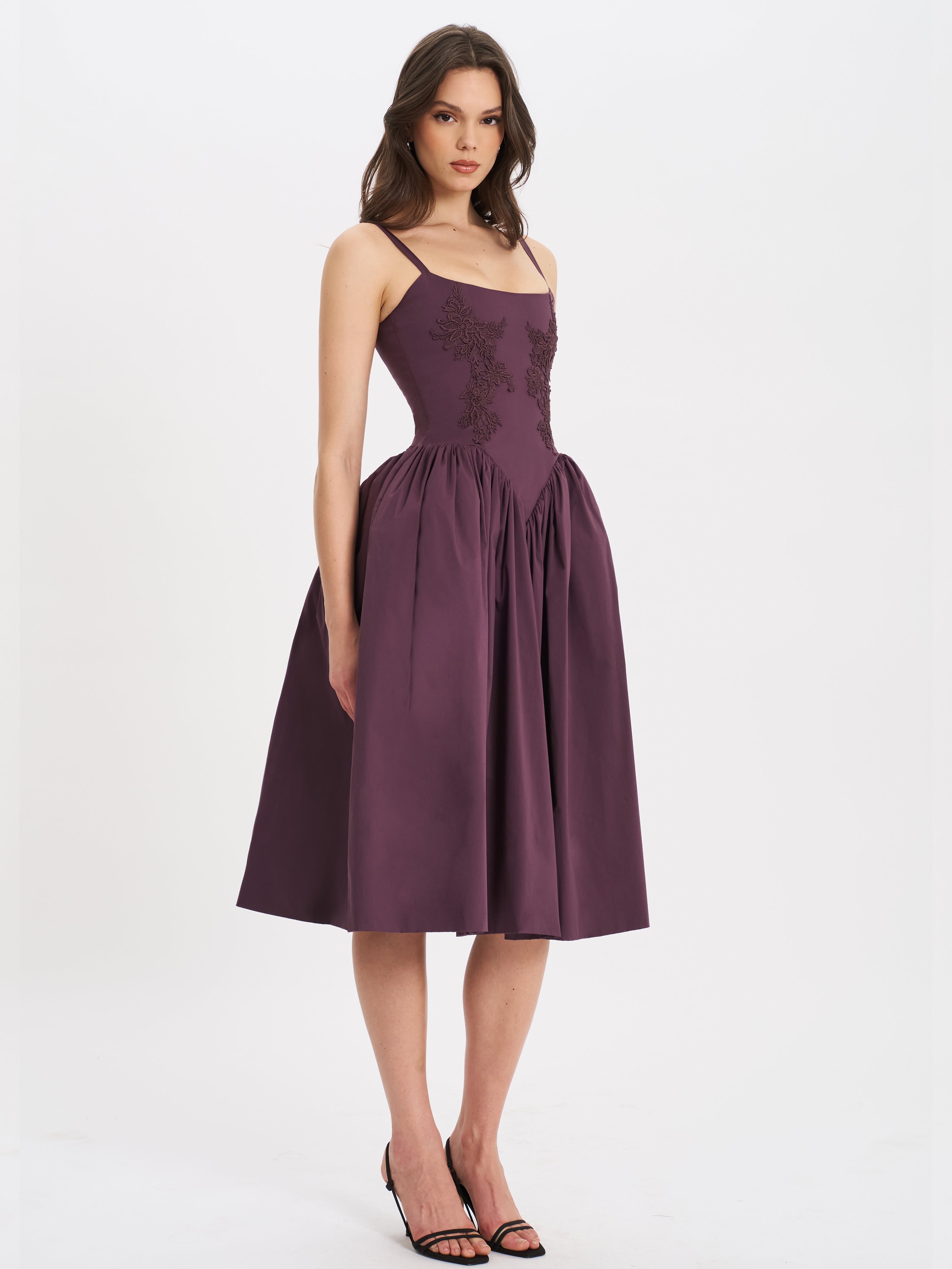 Side profile of woman wearing purple embroidered midi dress with elegant full skirt.