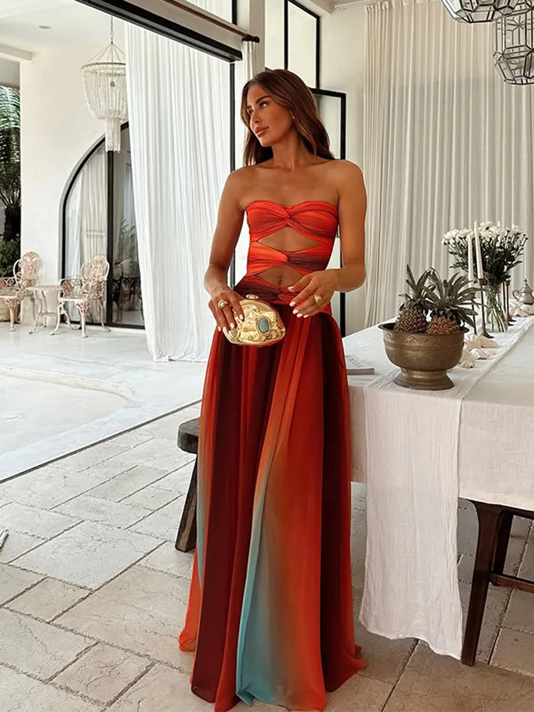 Full-length view of a strapless Callie Cutout Maxi Dress featuring a vibrant orange, red, and blue gradient with twisted bodice cutouts.