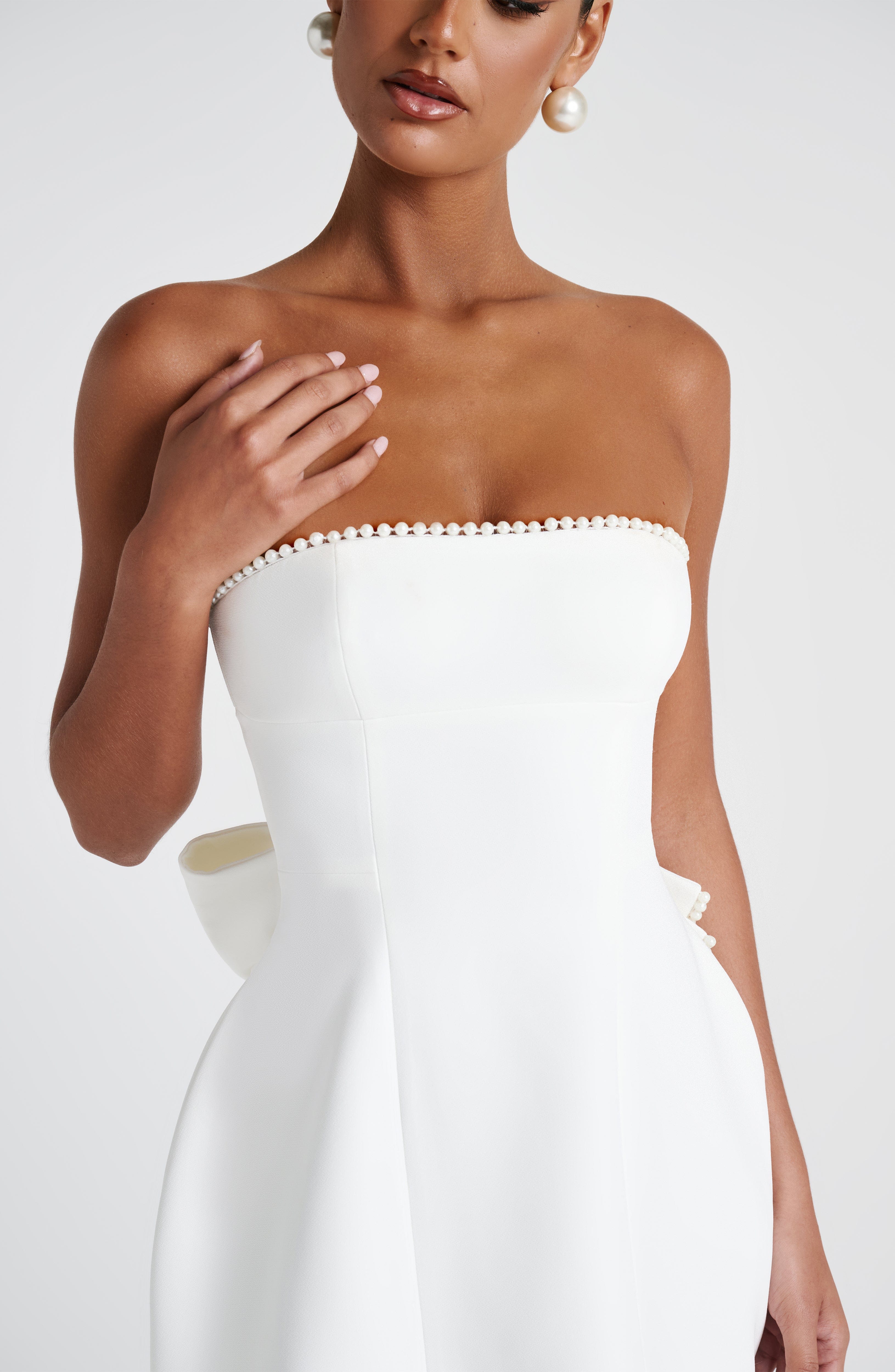 Close-up of the bodice of the white Calliope Pearl Bow Mini Dress, showing the pearl-embellished strapless neckline.