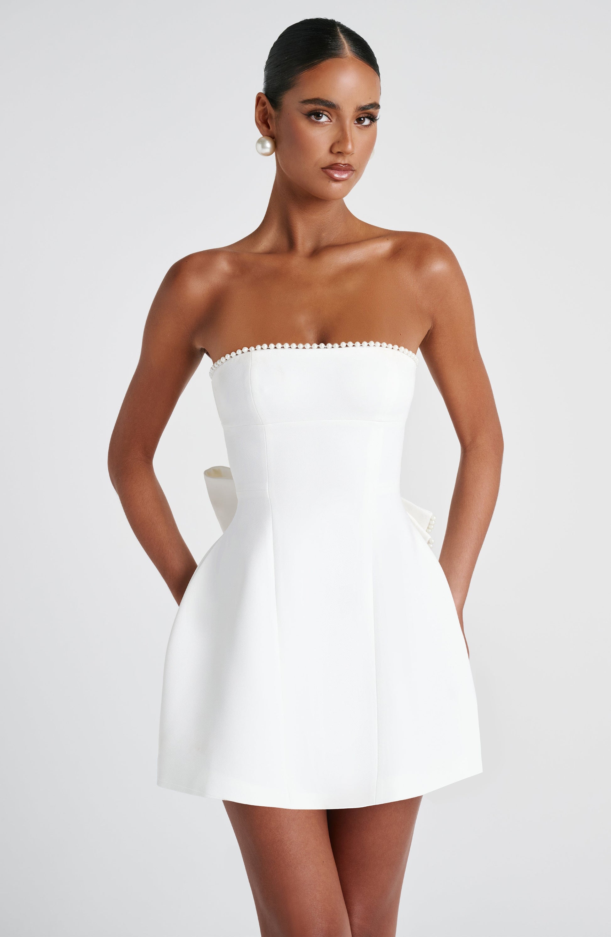 Front view of a white Calliope Pearl Bow Mini Dress with pearl trim along the strapless neckline.