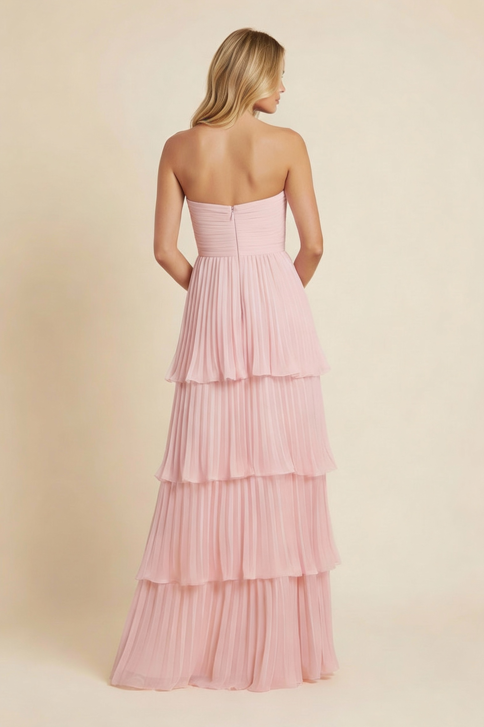 Back view of a woman wearing a light pink tiered maxi dress, showing the full pleated skirt and strapless back