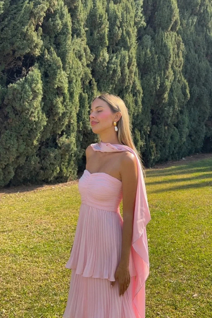 Front view of a light pink tiered maxi dress with a strapless ruched bodice and flowing pleated skirt