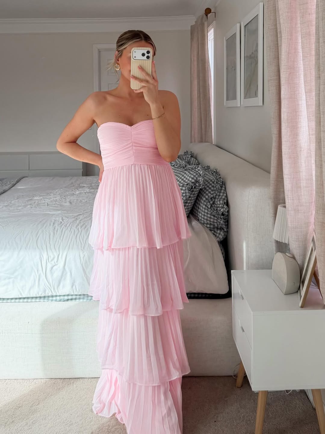 Indoor shot of a woman wearing a light pink tiered maxi dress with a strapless ruched top and pleated skirt