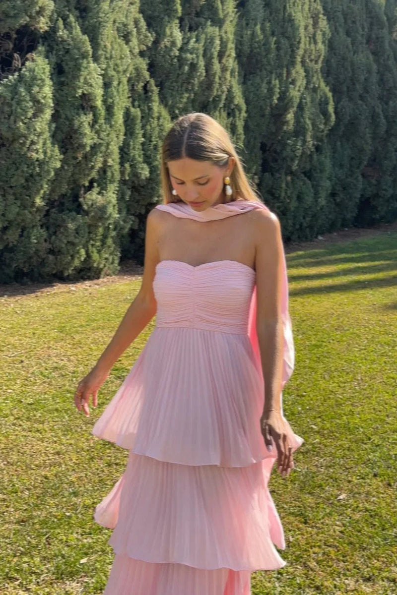 Front view of a light pink tiered maxi dress with a strapless ruched bodice and flowing pleated skirt